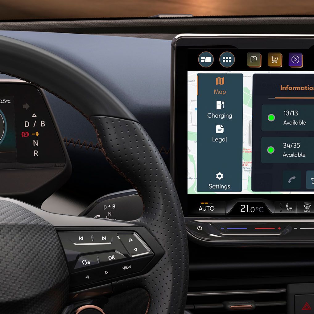 Prikaz notranjosti avtomobila CUPRA Born s fokusom na osrednji zaslon na dotik, ki prikazuje informacije o polnilnih postajah za električna vozila. Zaslon prikazuje podatke o razpoložljivosti, moči in ceni polnjenja. Na levi strani je volan s krmiljenjem in mehanizmom za prestavljanje.