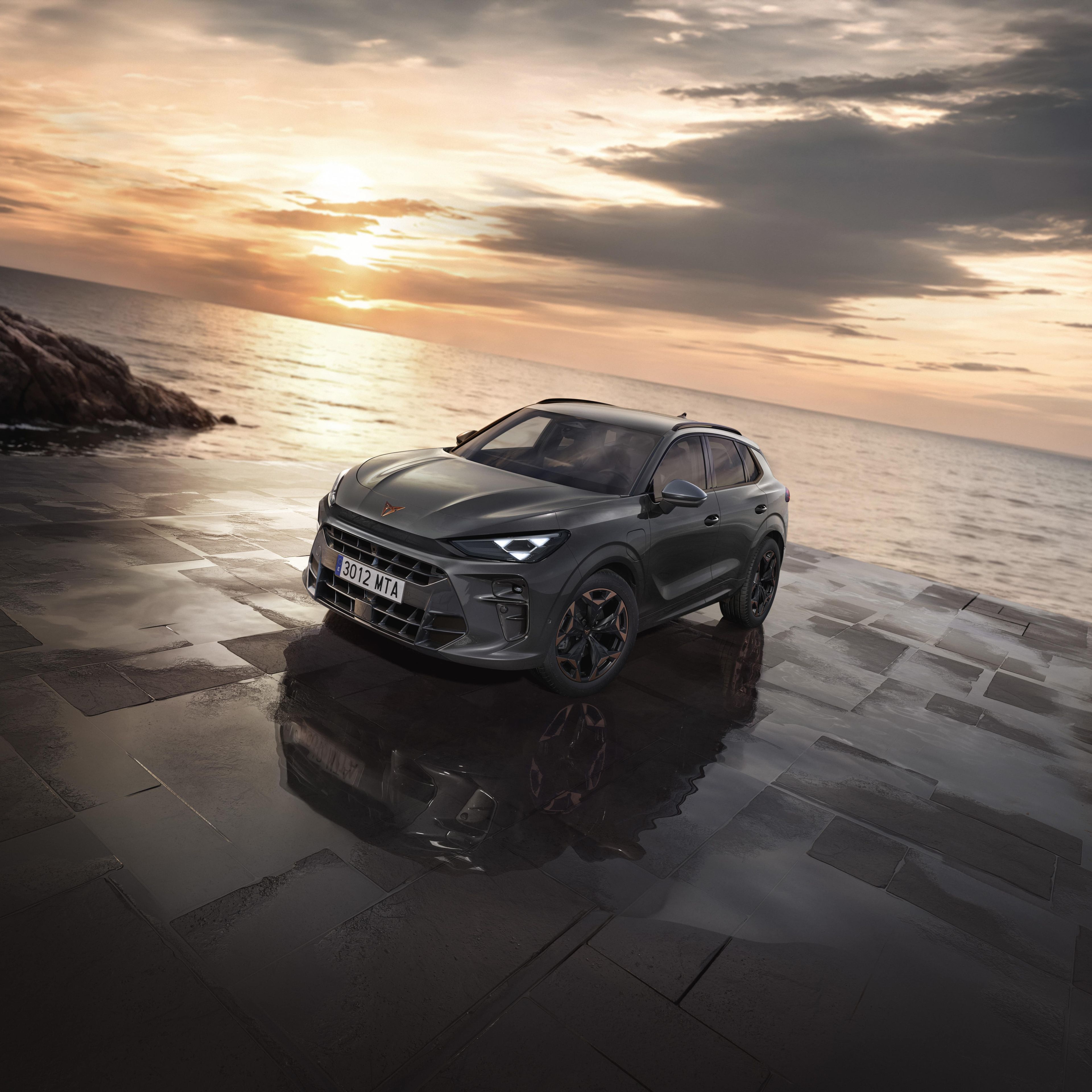 CUPRA Terramar je parkiran na tlakovani površini ob morju ob sončnem zahodu. Avto ima sodoben dizajn in črna platišča.