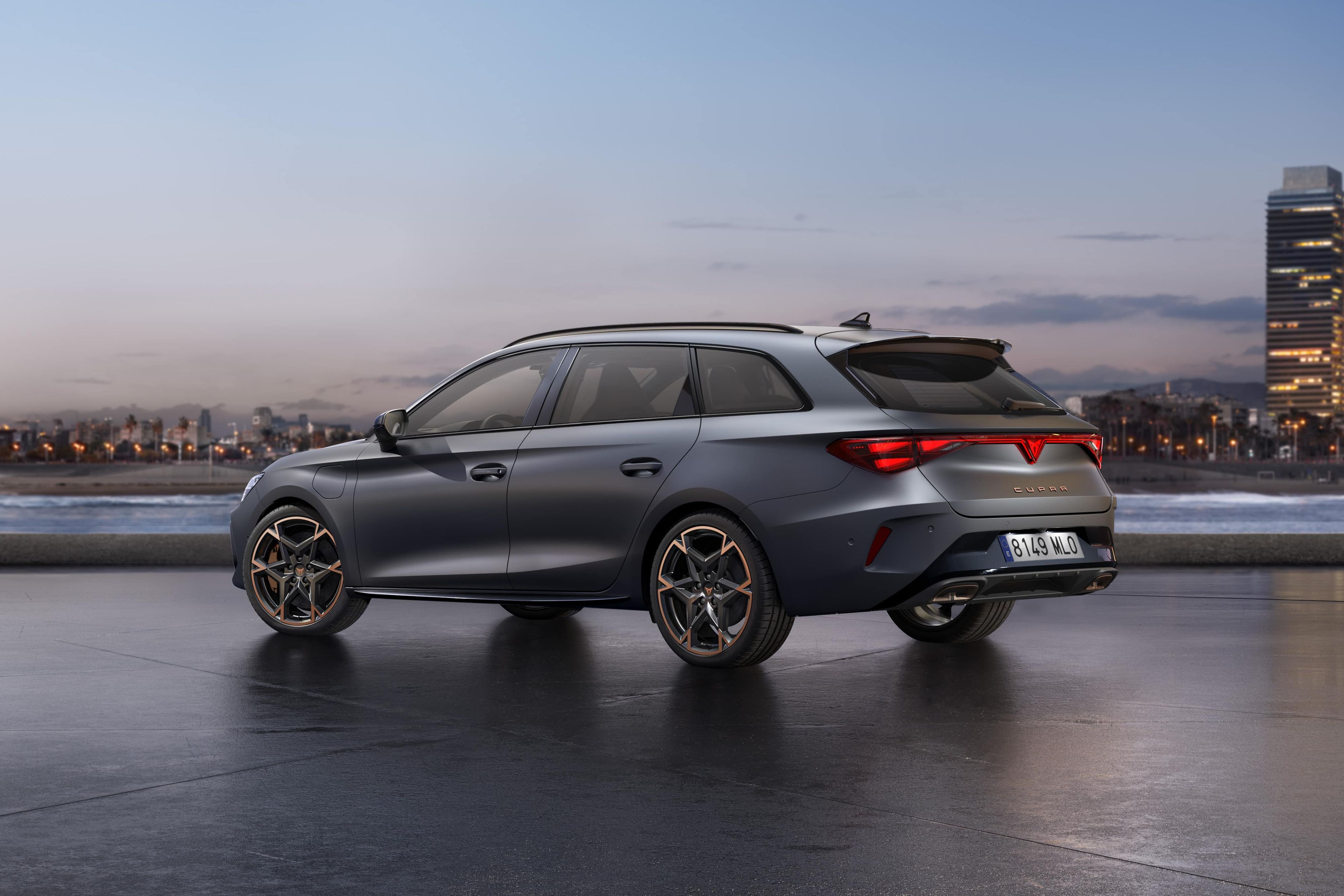 CUPRA LEON SPORTSTOURER stoji ob obali ob sončnem zahodu. V ozadju je mestno obzorje z visokimi stavbami, mokra površina pod vozilom pa odseva nebo.