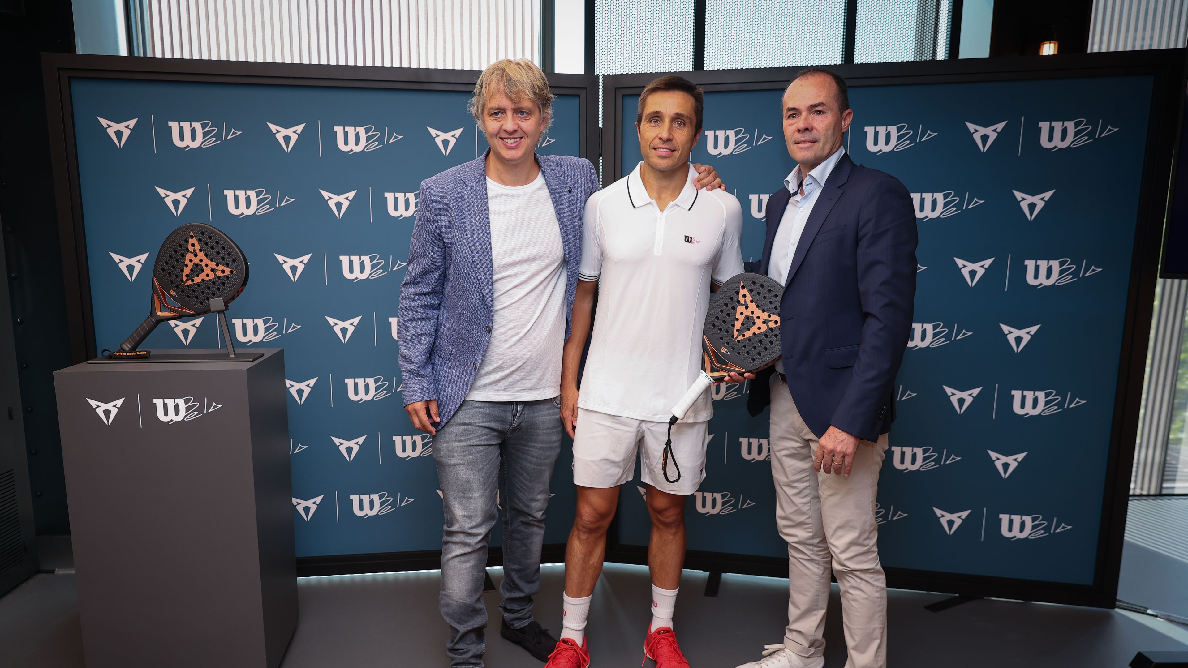 Ignasi Prieto, Fernando Belasteguín in tretji moški stojijo pred steno z logotipi CUPRA, Wilson in Bela. En moški drži črni lopar za padel z logotipom znamke CUPRA. 