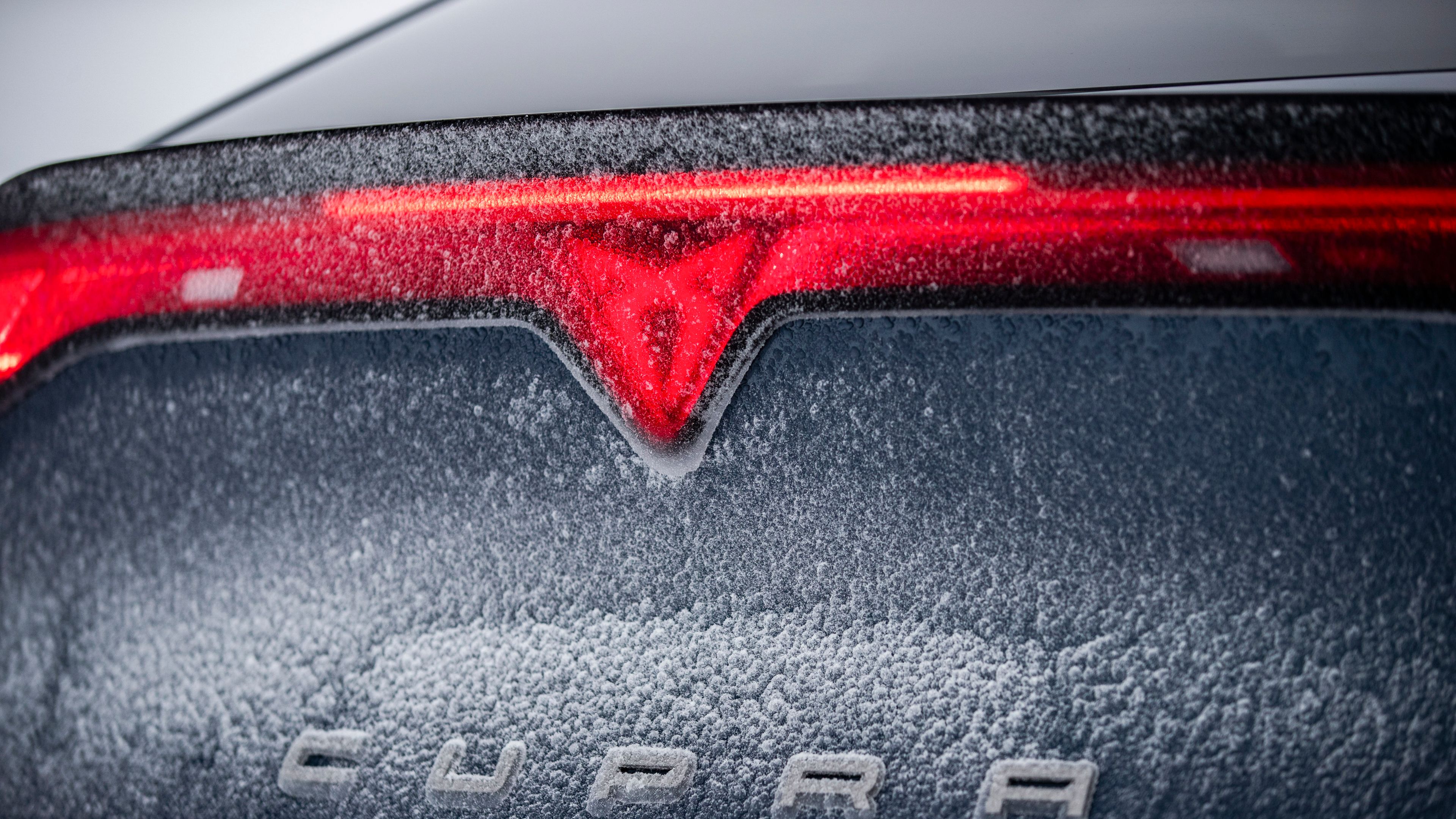 Zadnji del avtomobila Cupra Tavascan, prekrit s snegom in ledom. Vidna je rdeča luč in logotip CUPRA.