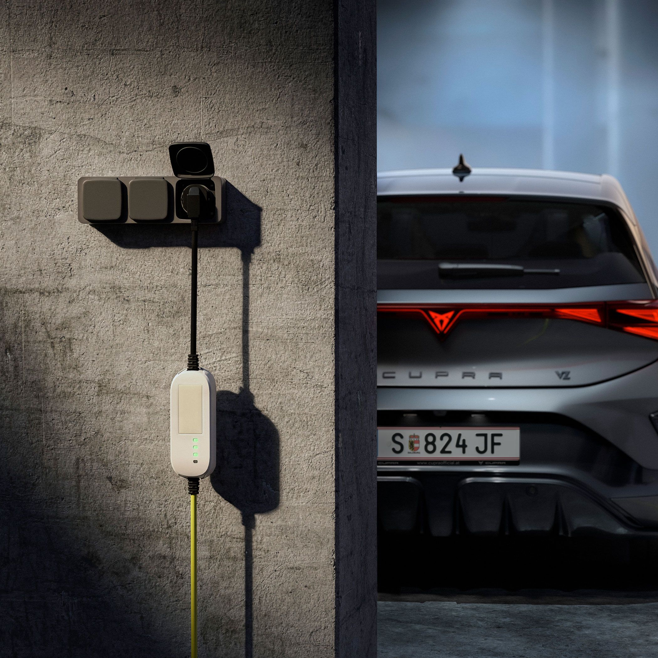 Električni avto CUPRA BORN je parkiran v garaži in priključen na stensko polnilno postajo z rumenim kablom. Leva stran slike prikazuje siv betonski zid z nameščenim polnilnikom, desna pa zadnji del avtomobila s prižganimi zadnjimi lučmi. V ozadju je zamegljen, industrijsko videti prostor.