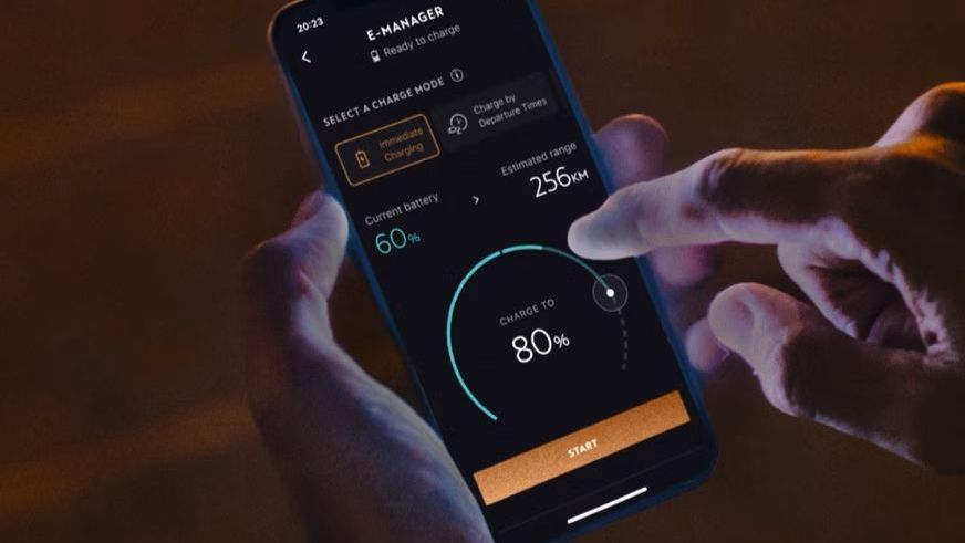 Oseba drži pametni telefon in uporablja aplikacijo 'My CUPRA app' za upravljanje polnjenja baterije električnega vozila. Zaslon prikazuje trenutni nivo baterije in možnost polnjenja do določenega odstotka.