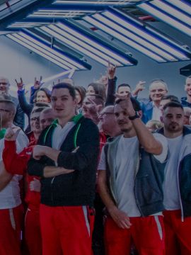 Velika skupina ljudi stoji okoli avtomobila znamke CUPRA v osvetljeni hali. Avtomobil je osrednji del fotografije.