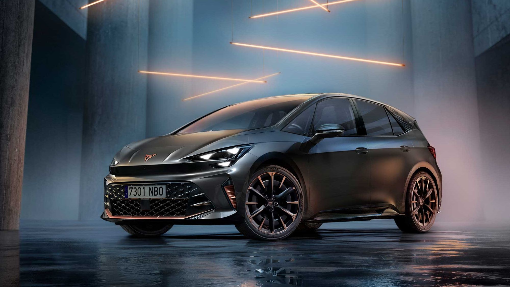 Temno siv CUPRA Born stoji v futurističnem, zatemnjenem prostoru z visokimi betonskimi stebri. Nad njim visijo tanki oranžni svetlobni trakovi, ki osvetljujejo bleščečo karoserijo in kovinska platišča. 