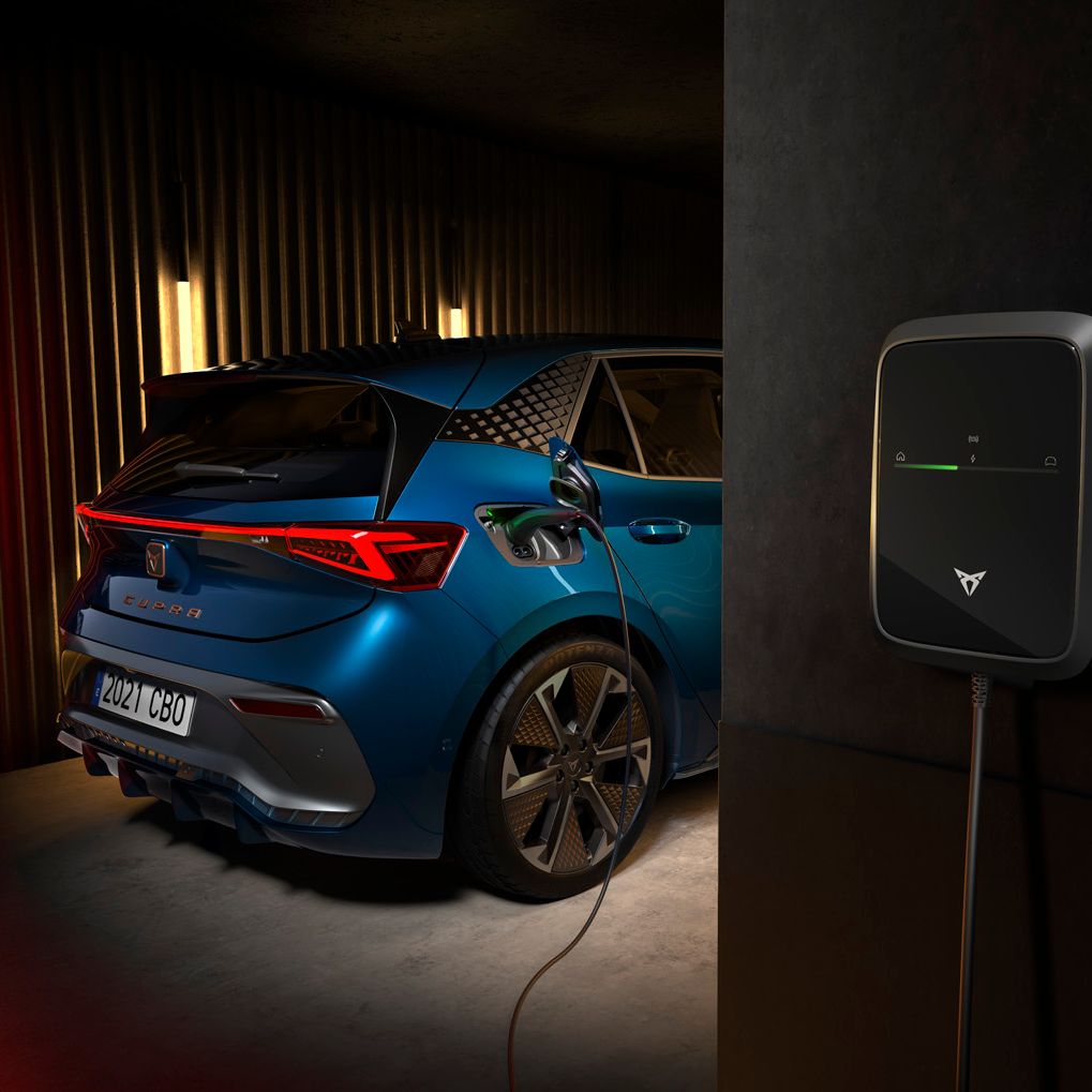 Električni avtomobil CUPRA Born je priključen na polnilno postajo v garaži. Avto je modre barve in ima športne značilnosti. Polnilna postaja je nameščena na steni.