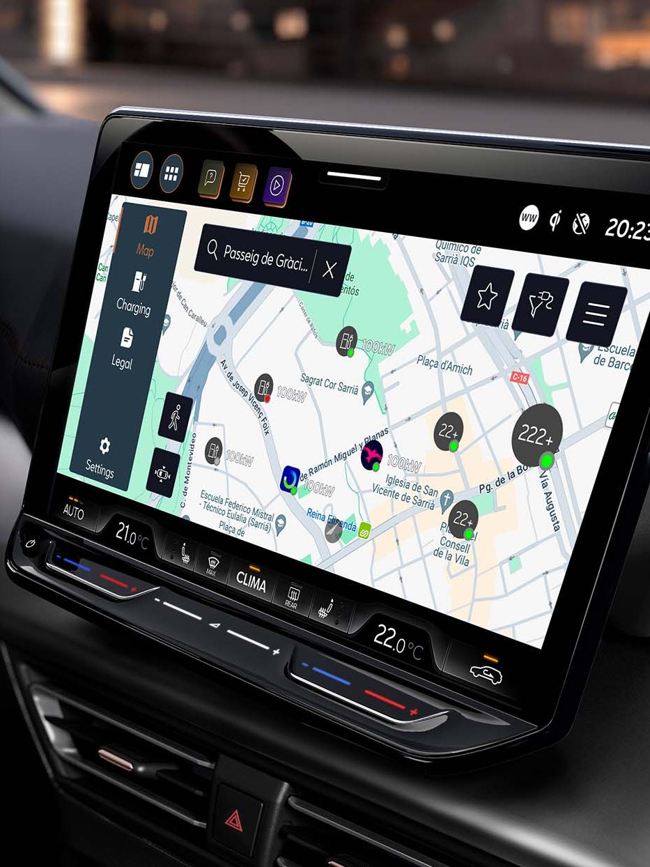 Notranjost sodobnega avtomobila CUPRA Born prikazuje volan in velik zaslon, na katerem je navigacijski sistem z zemljevidom. Osvetljena so mesta in točke zanimanja na zaslonu. V ozadju je vidno mesto ponoči.