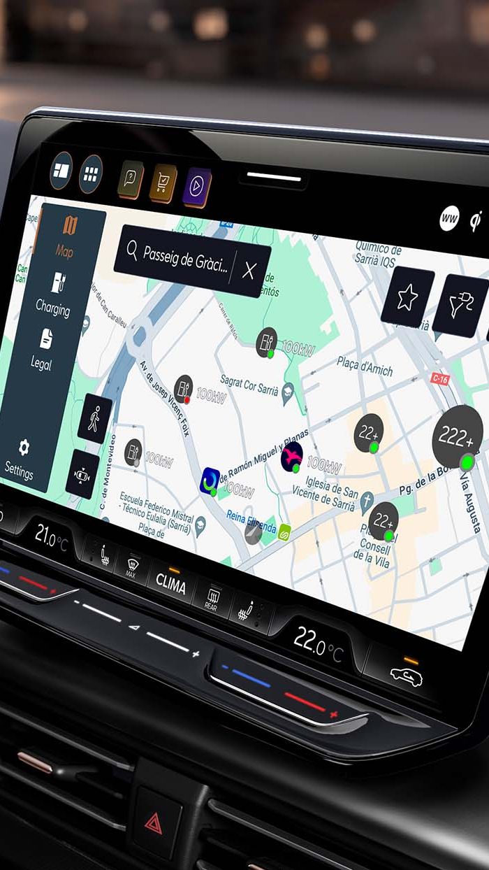 Notranjost sodobnega avtomobila CUPRA Born prikazuje volan in velik zaslon, na katerem je navigacijski sistem z zemljevidom. Osvetljena so mesta in točke zanimanja na zaslonu. V ozadju je vidno mesto ponoči.