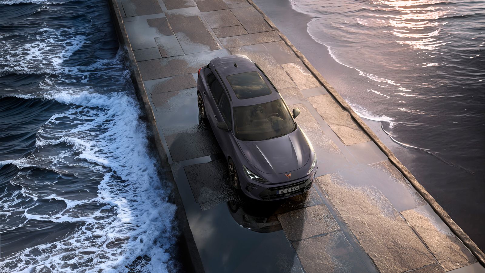 Hibridni SUV Cupra Terramar 2024 na mokrem vozišču ob morju, z elegantnimi žarometi, sodobnimi aluminijastimi platišči in animalističnim sprednjim delom.