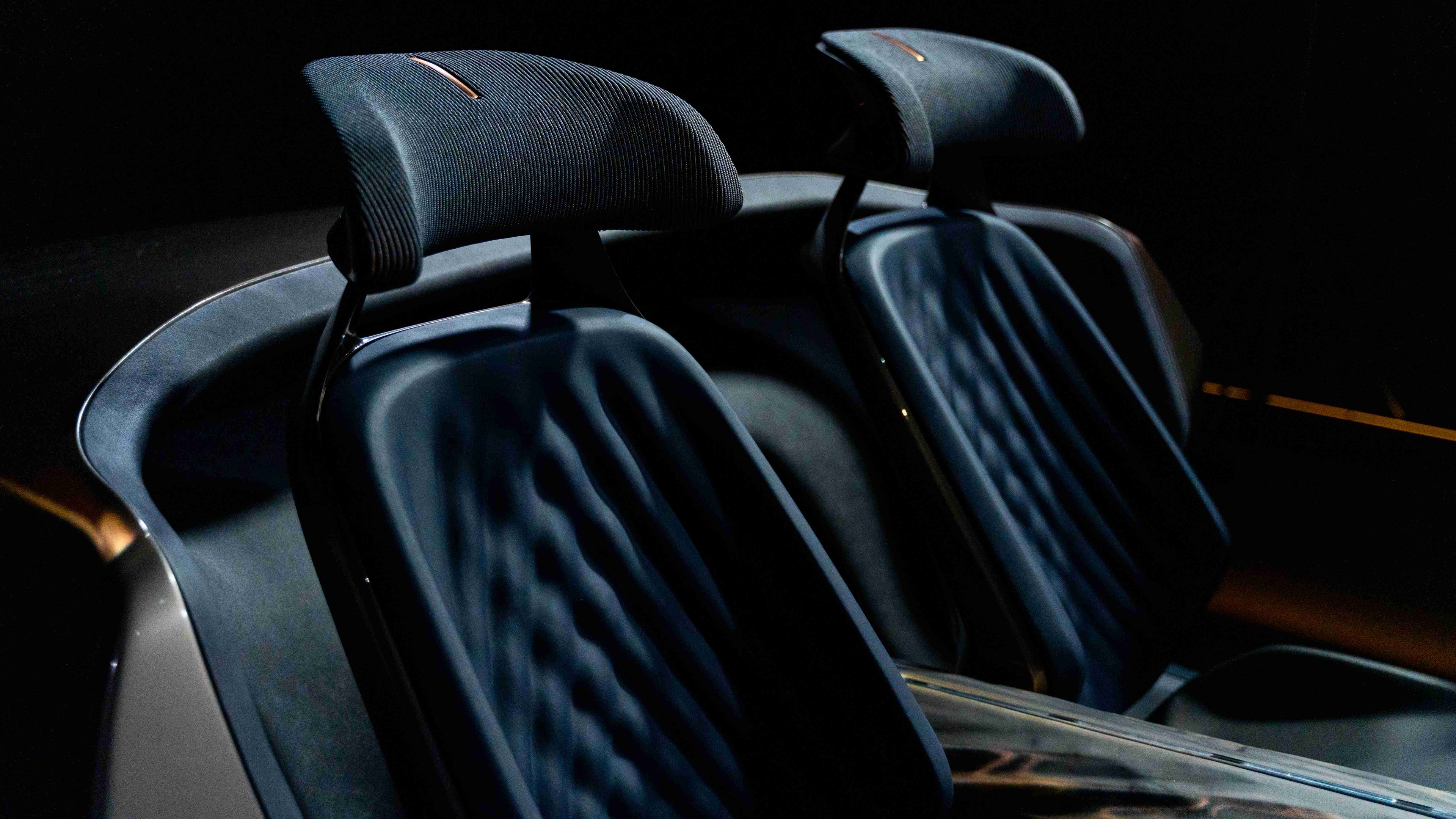 Usnjena sedeža športnega avtomobila z visokimi nasloni za glavo sta osvetljena v temnem ambientu. Na sedežih so vidne elegantne gube in detajli.