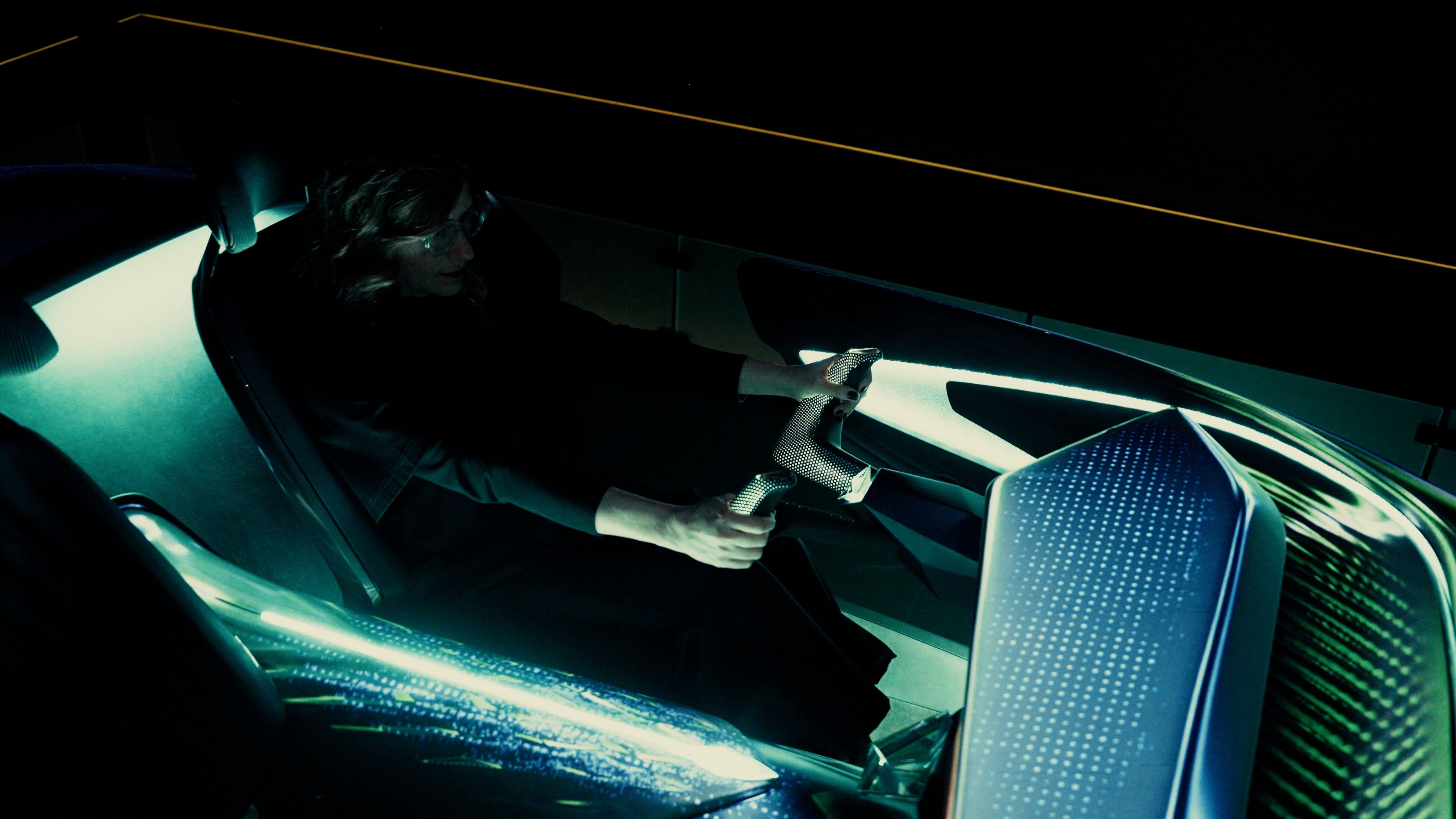 Oseba sedi v futurističnem vozilu z osvetljenimi notranjimi elementi. Roke ima na volanu oblikovanem kot krmilo. Vozilo je visokotehnološko in ima stekleno streho.