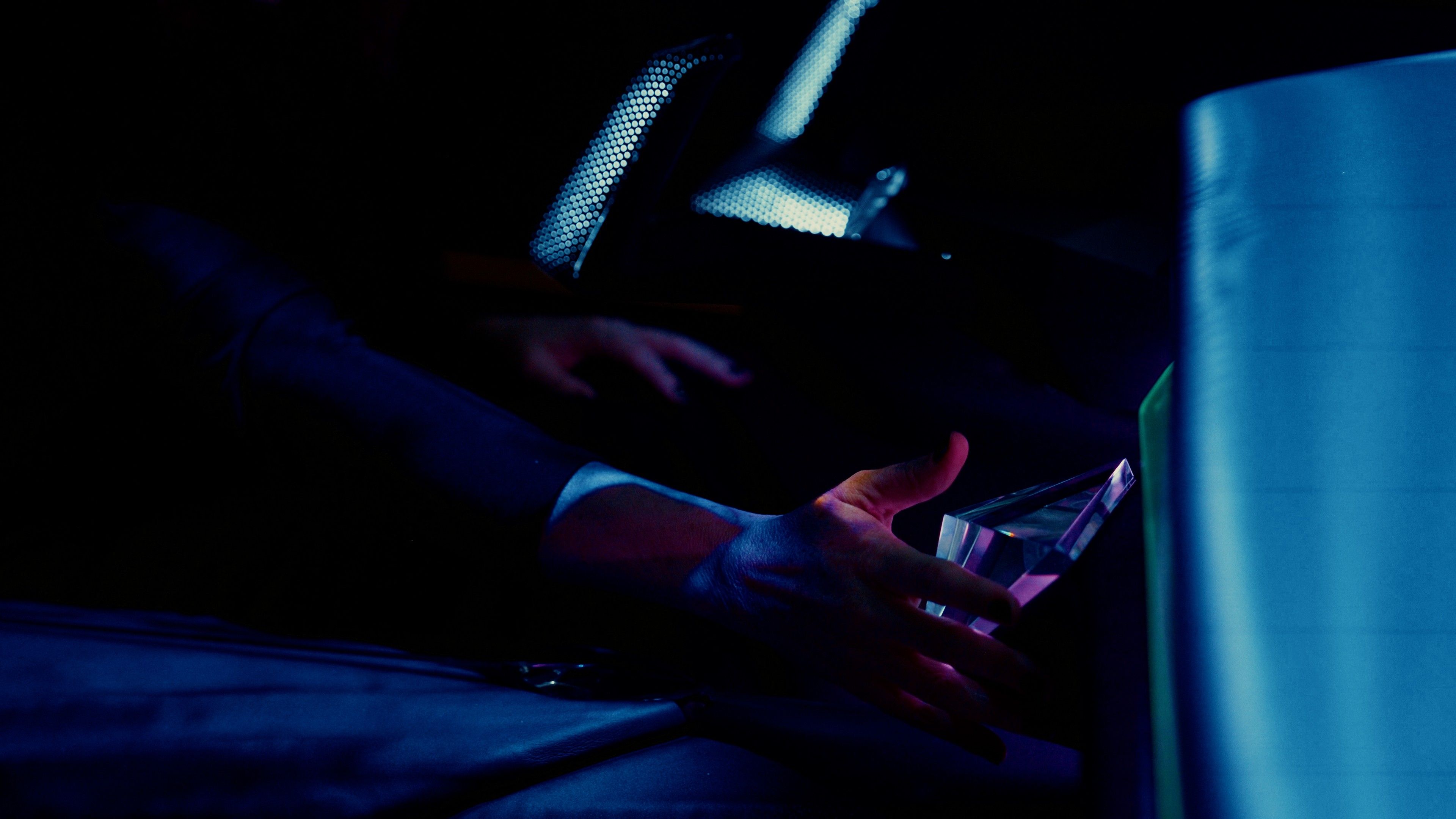 Oseba v temi drži prozoren menjalnik. Oseba sedi in je obkrožena z modro osvetlitvijo.