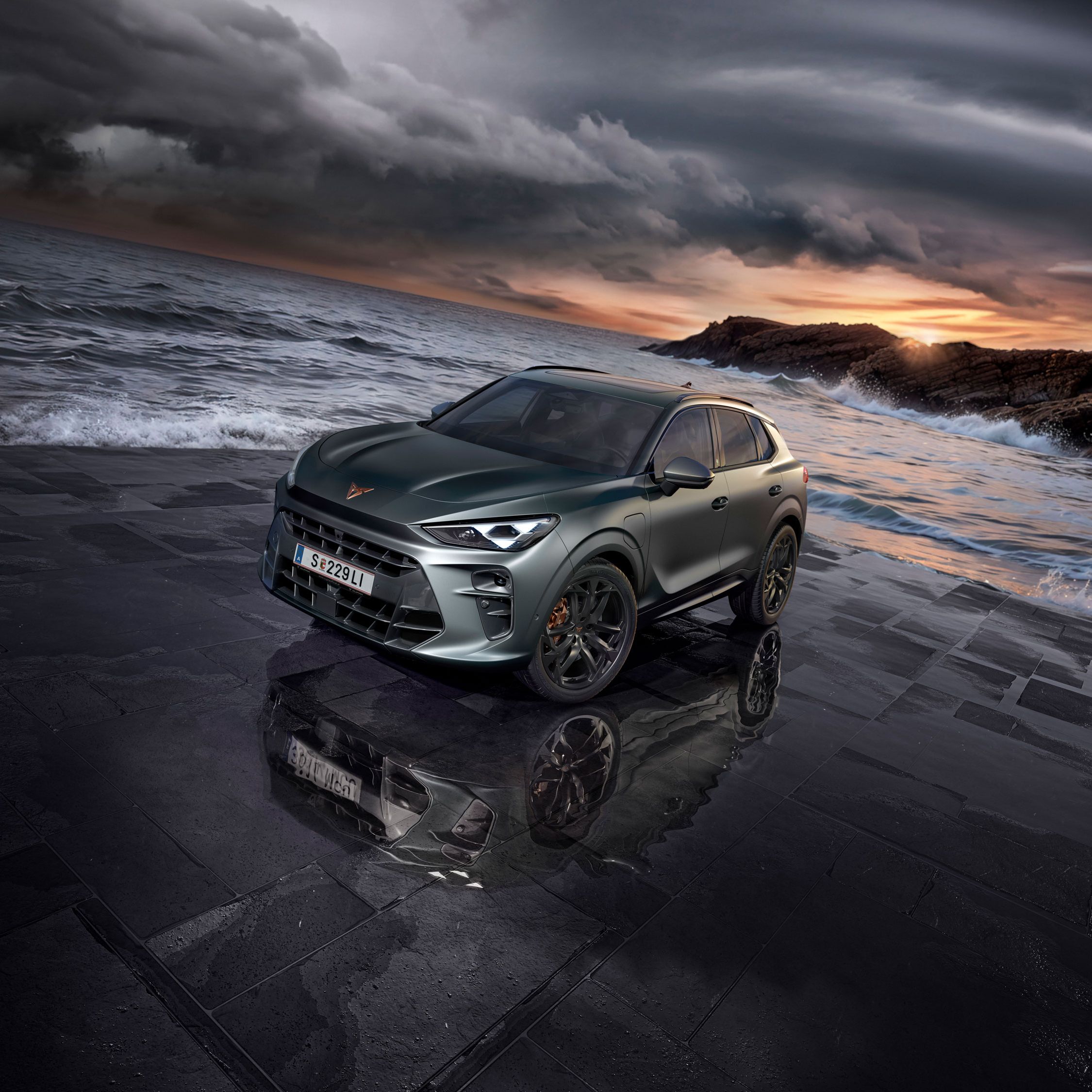 Sodobna temno sivo vozilo CUPRA Terramar, s črnimi platišči, na mokrem tlakovcu ob obali z oblačnim nebom v ozadju. Morje, valovi in skalnata obala se raztezajo v ozadju.