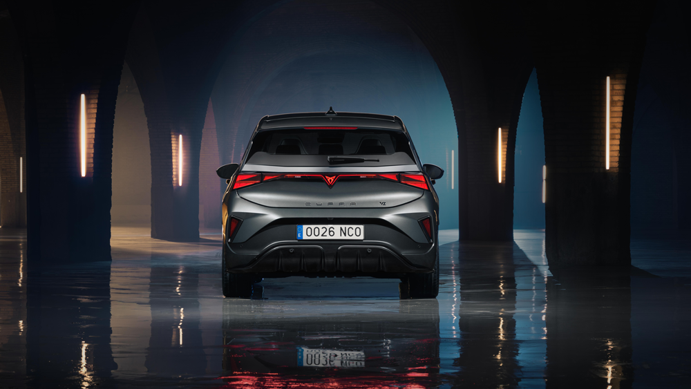 CUPRA Born VZ od zadaj v simetričnem pogledu v arhitekturnem ambientu z dramatično osvetlitvijo. Refleksija na tleh poudarja eleganco vozila.