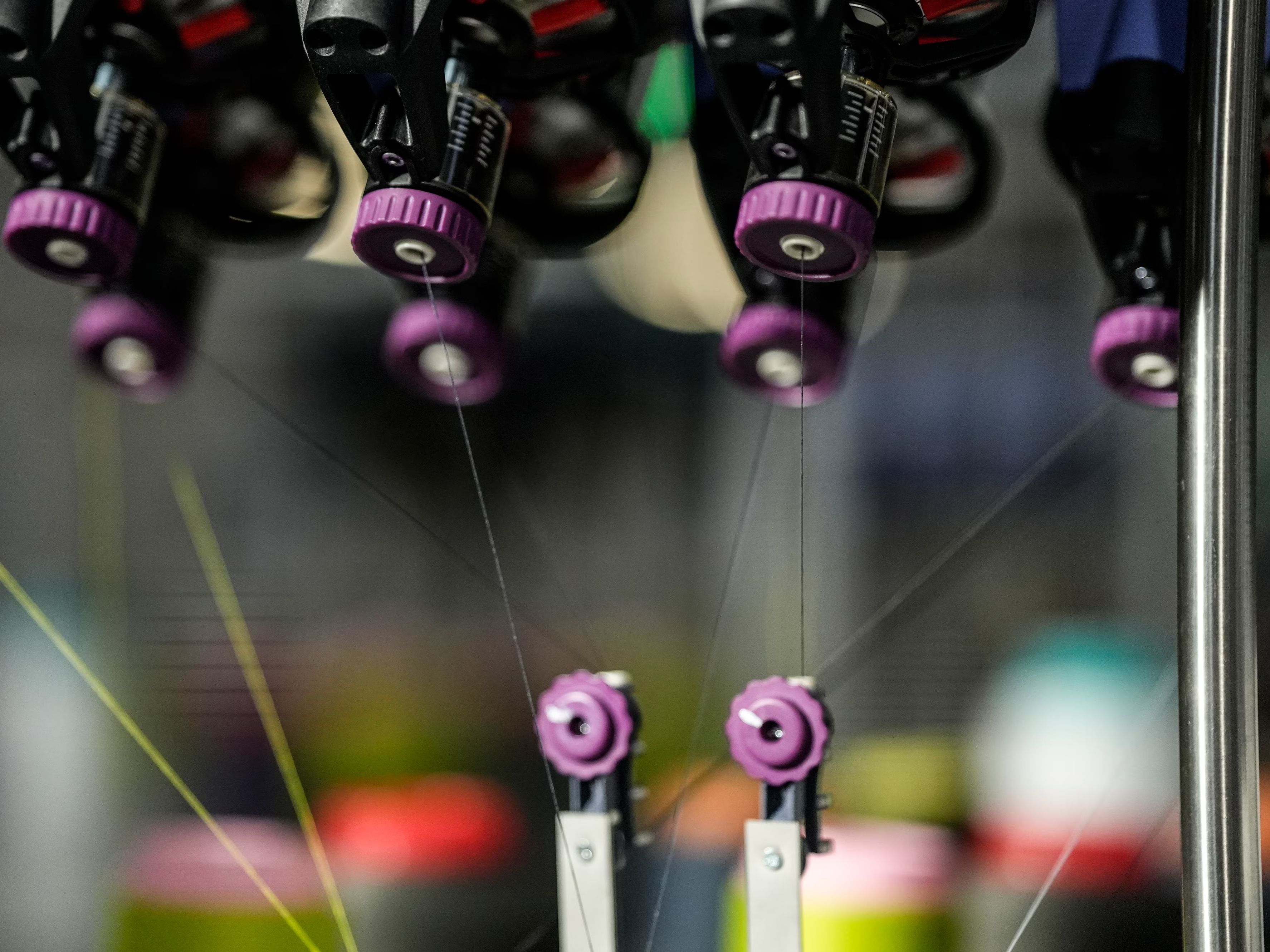 Detajl 3D industrijskega stroja, kjer se več niti vodi skozi mehanske vodila in šobe. Prizor prikazuje natančen in avtomatiziran proces izdelave tekstilnih materialov.