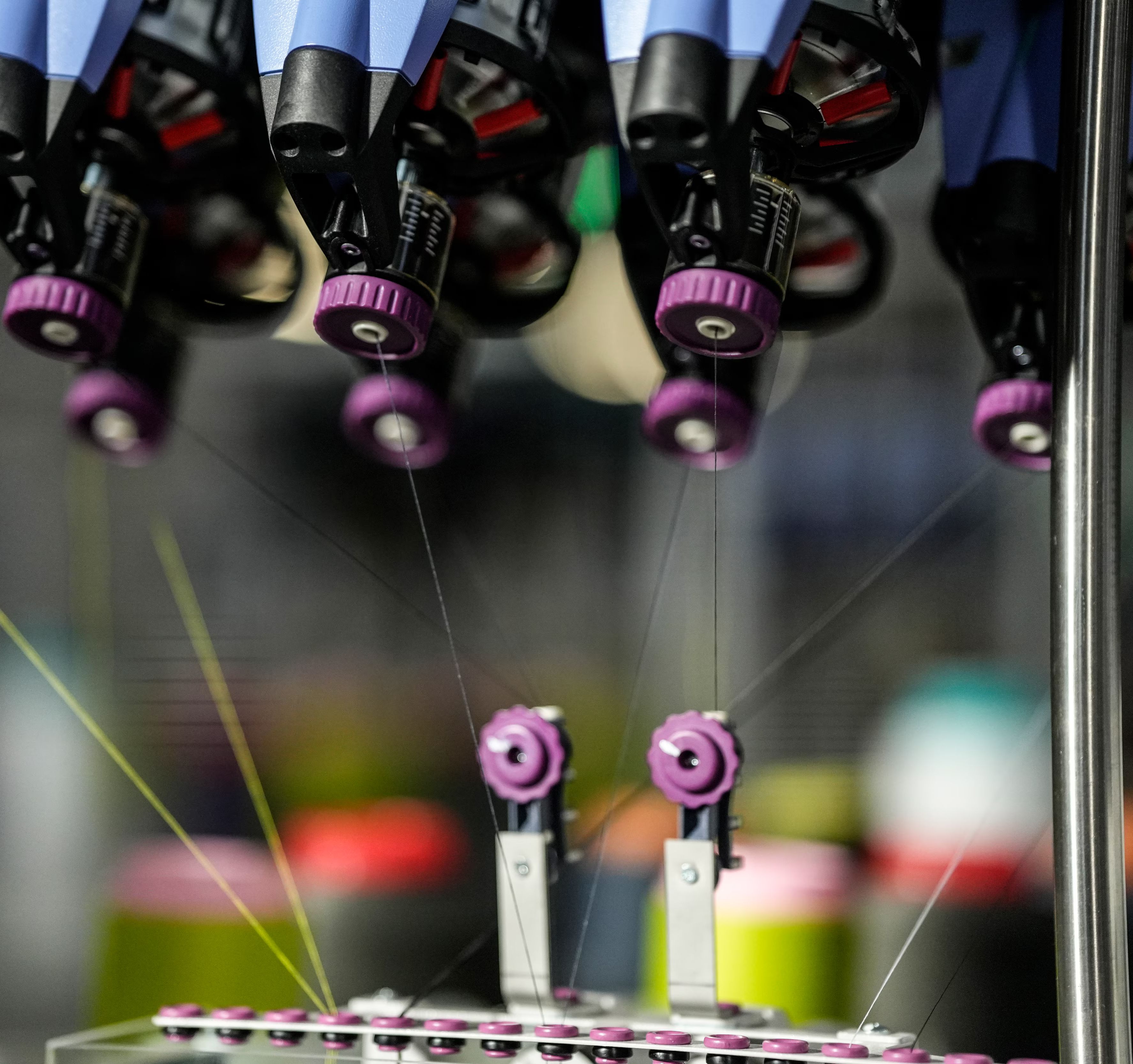 Detajl 3D industrijskega stroja, kjer se več niti vodi skozi mehanske vodila in šobe. Prizor prikazuje natančen in avtomatiziran proces izdelave tekstilnih materialov.