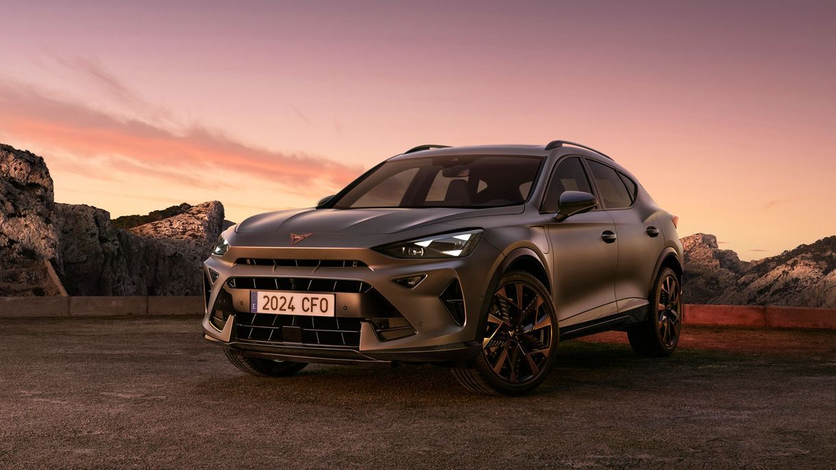Kamnita dolina in gorski hribi ob sončnem zahodu z elegantnim CUPRA Formentor PA – PHEV VZ v ospredju. Temno sivo vozilo je obrnjeno proti kameri.
