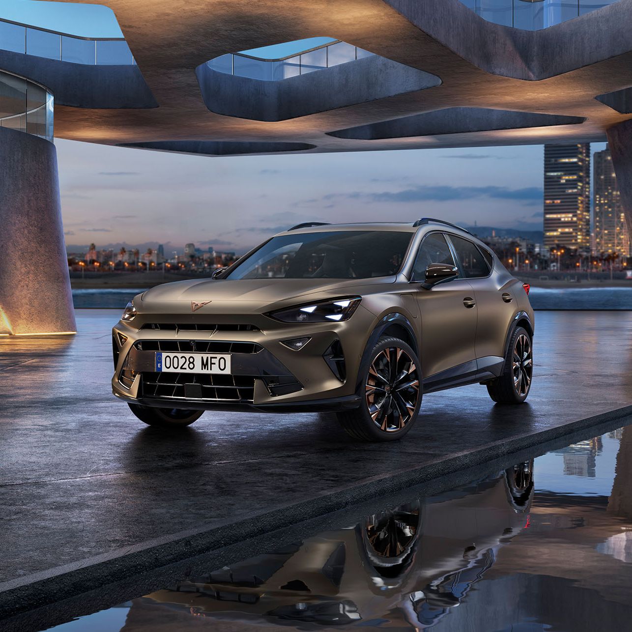 CUPRA Formentor PA je parkiran pod sodobno arhitekturo z velikimi ukrivljenimi betonskimi strukturi. Vozilo ima elegantne linije in kovinsko barvo. V ozadju je vidno osvetljeno mesto ob vodi.
