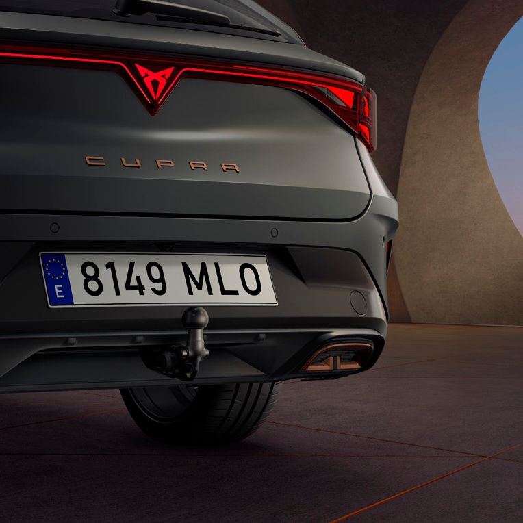 Na sliki je zadnji del avtomobila CUPRA LEON PA SP. Avtomobil je temno sive barve in ima rdeče zadnje luči. V ozadju je moderna betonska struktura.