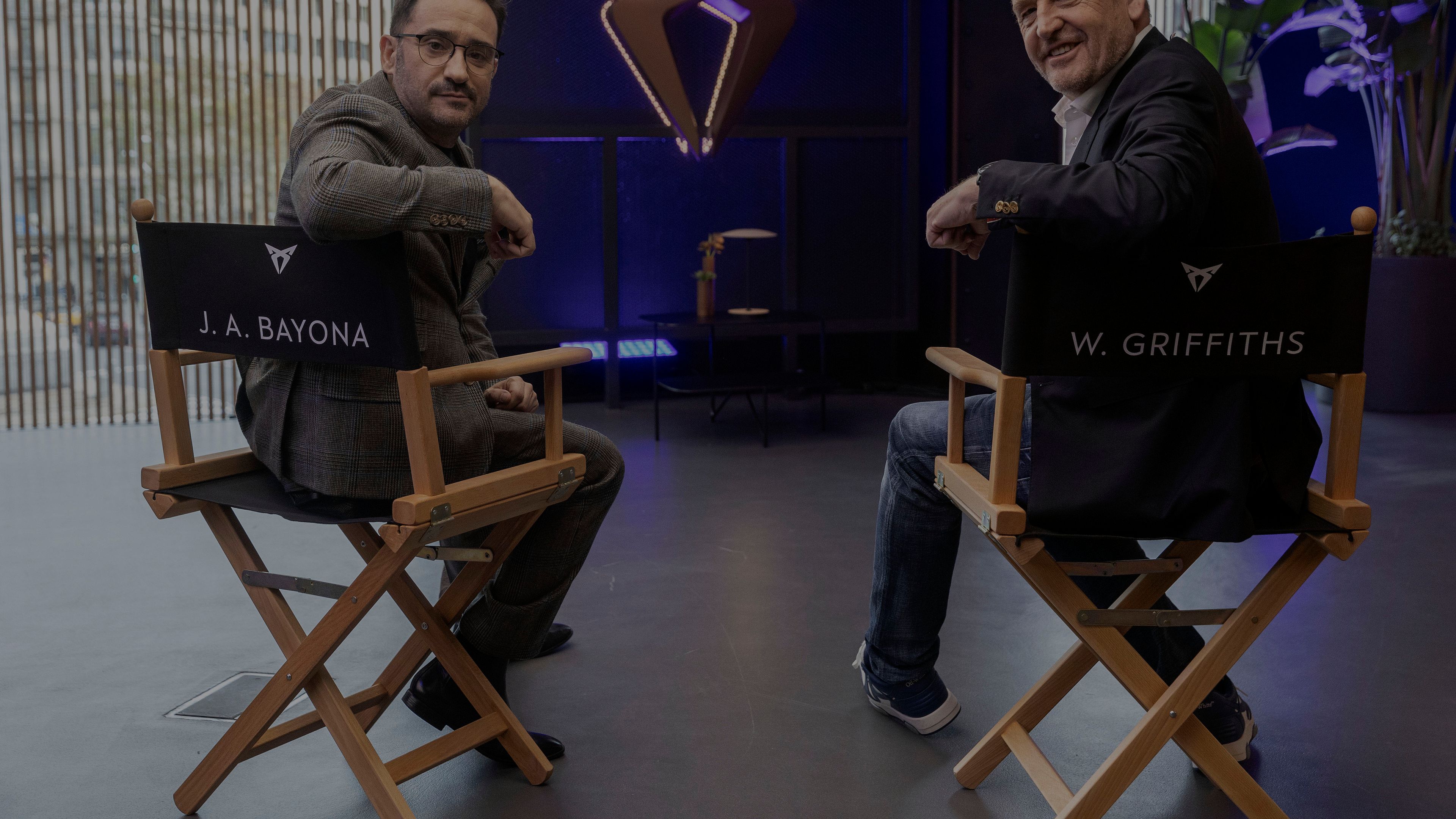 J. A. Bayona in W. Griffiths sedita na režiserskih stolih v sodobnem studiu, v ozadju pa je logotip znamke CUPRA.