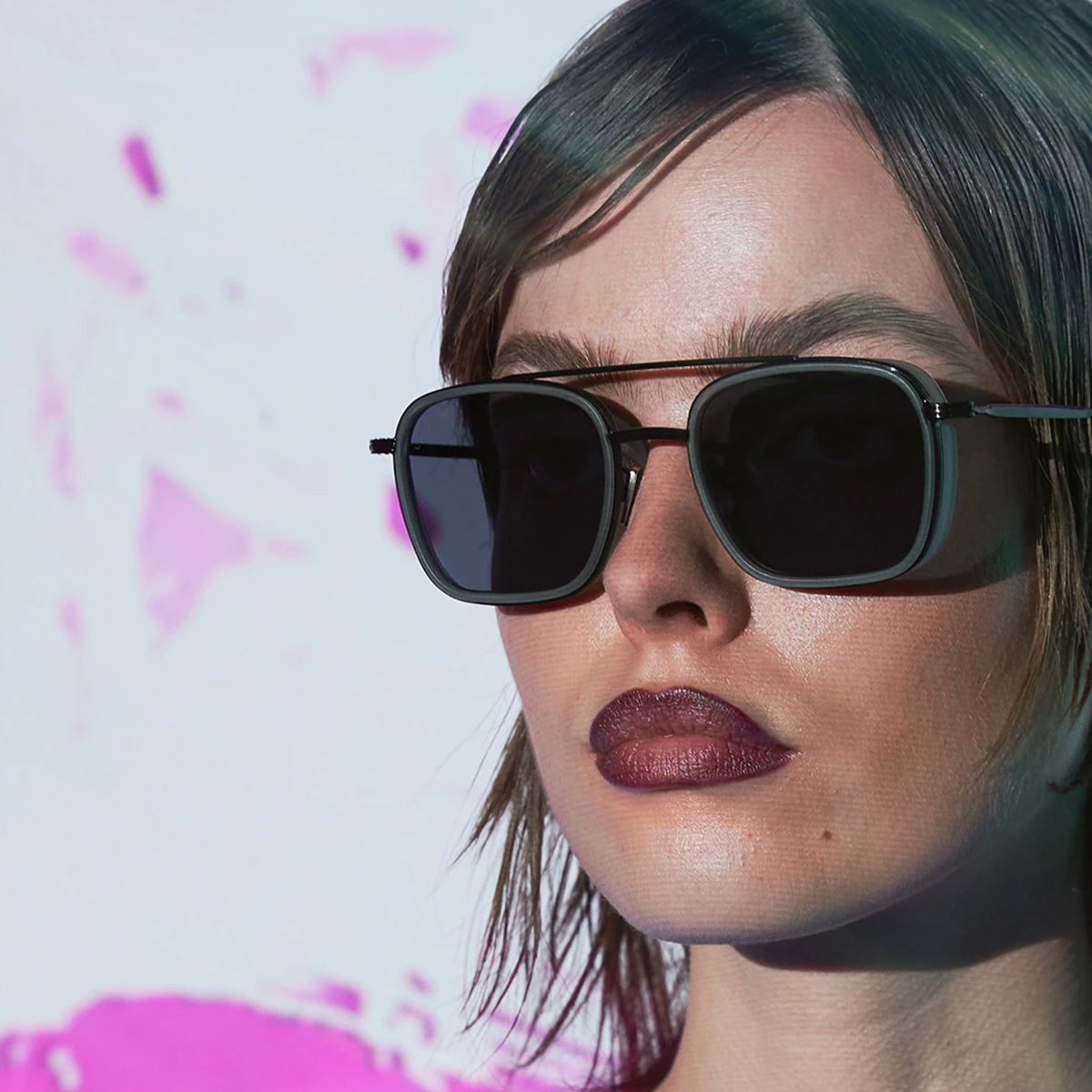 Ženska nosi sodobna CUPRA sončna očala. Zaledje je svetle barve s poudarki roza odtenkov.