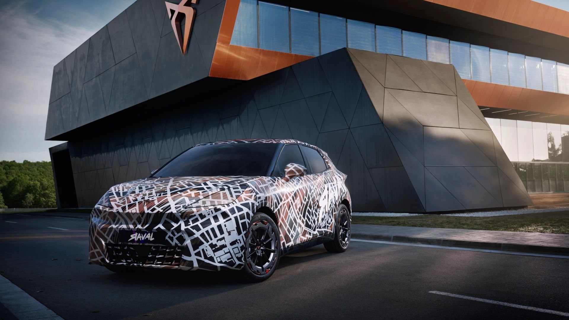 CUPRA Raval Dynamic, prekrit z kamuflažnimi vzorci, je parkiran pred modernim steklenim stavbo. V ozadju je logotip znamke CUPRA. 