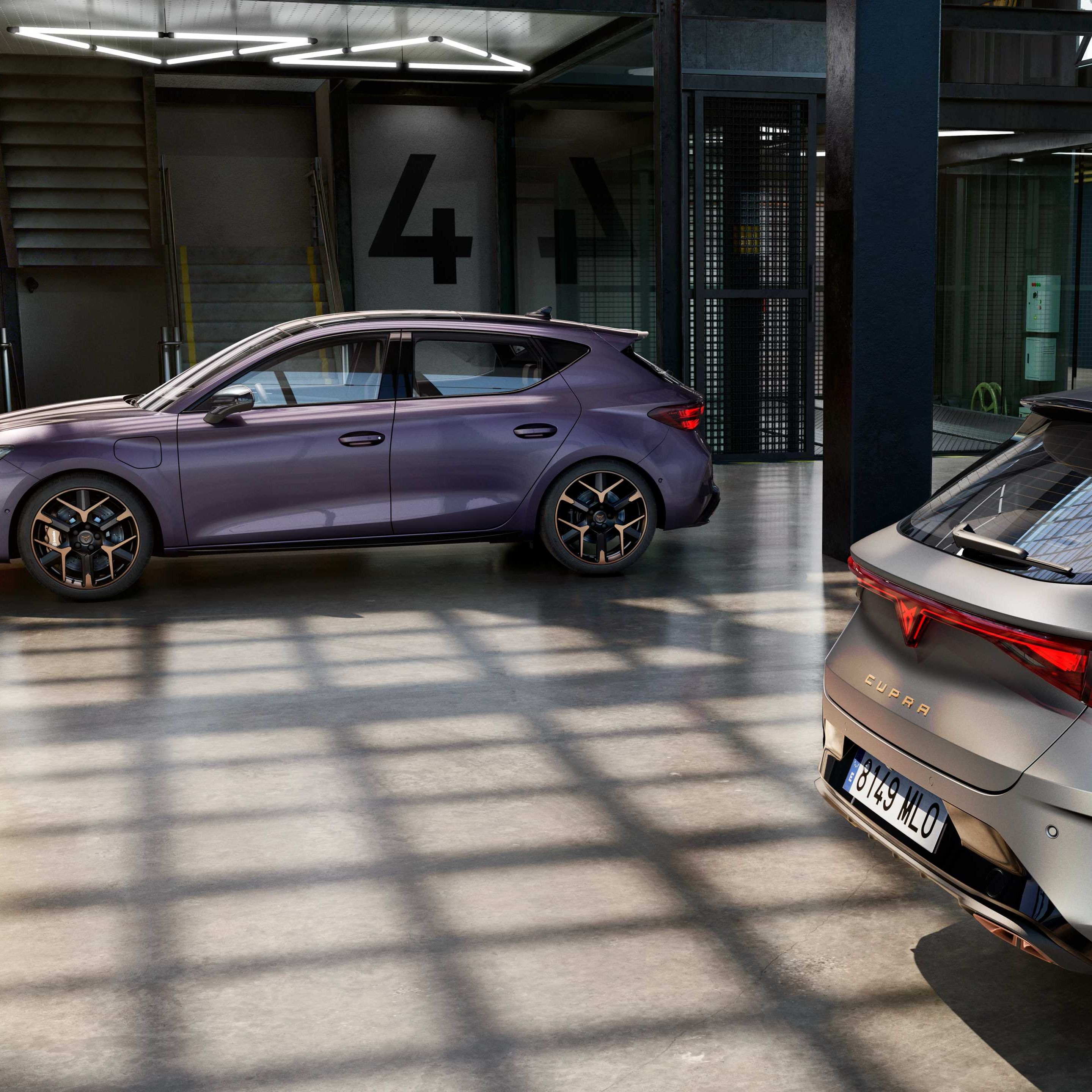 V industrijski garaži sta parkirana dva sodobna avtomobila znamke CUPRA. Eden je vijoličaste barve, drugi siv. Garaža ima velike steklene stene, skozi katere sije sončna svetloba.