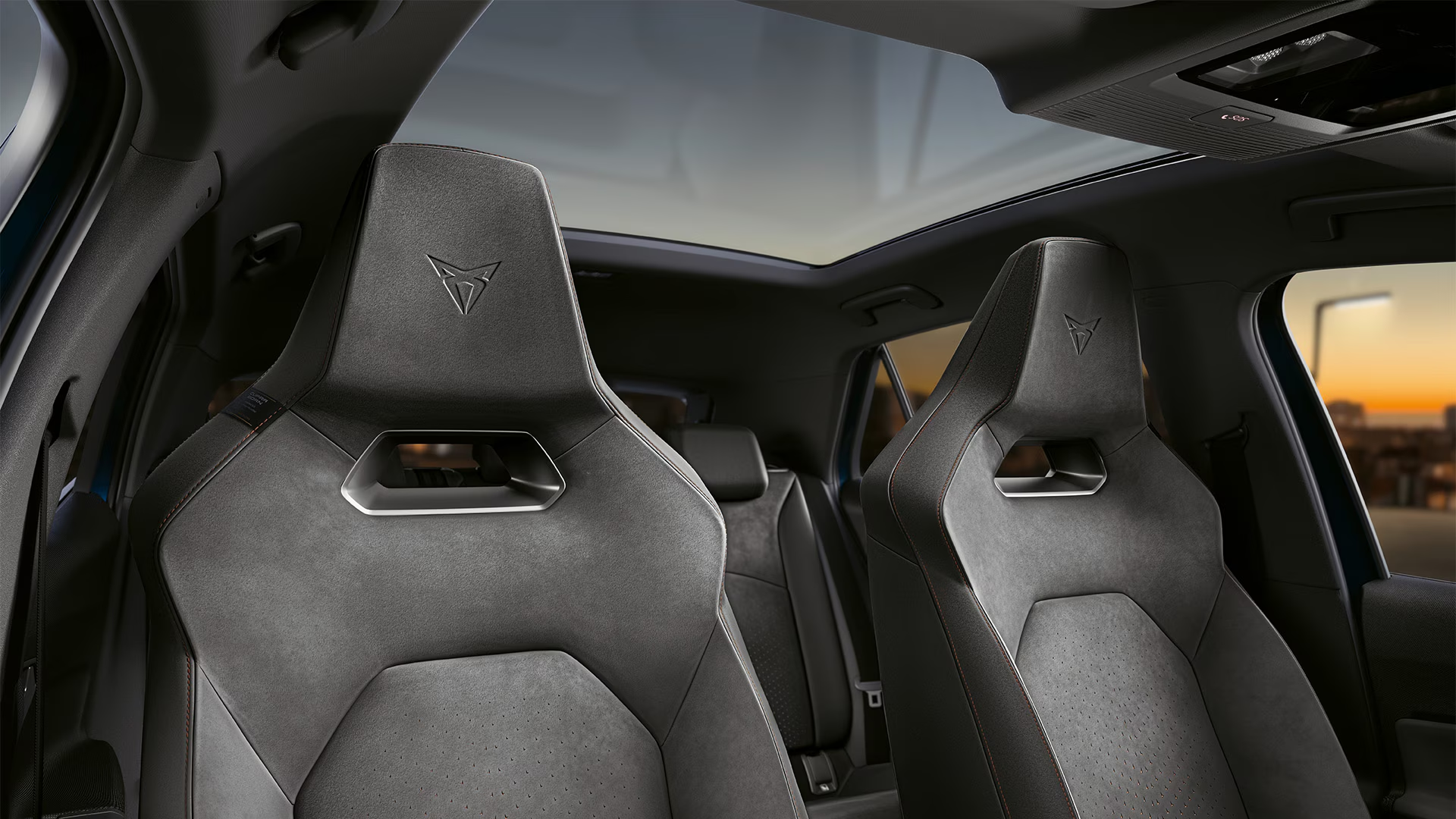 Notranjost avtomobila Cupra Raval prikazuje sprednja sedeža iz temnega blaga z elegantnim dizajnom in strešnim oknom. Sedeži imajo športni videz z izrazitimi linijami in informacijsko kontrolno ploščo na strehi.