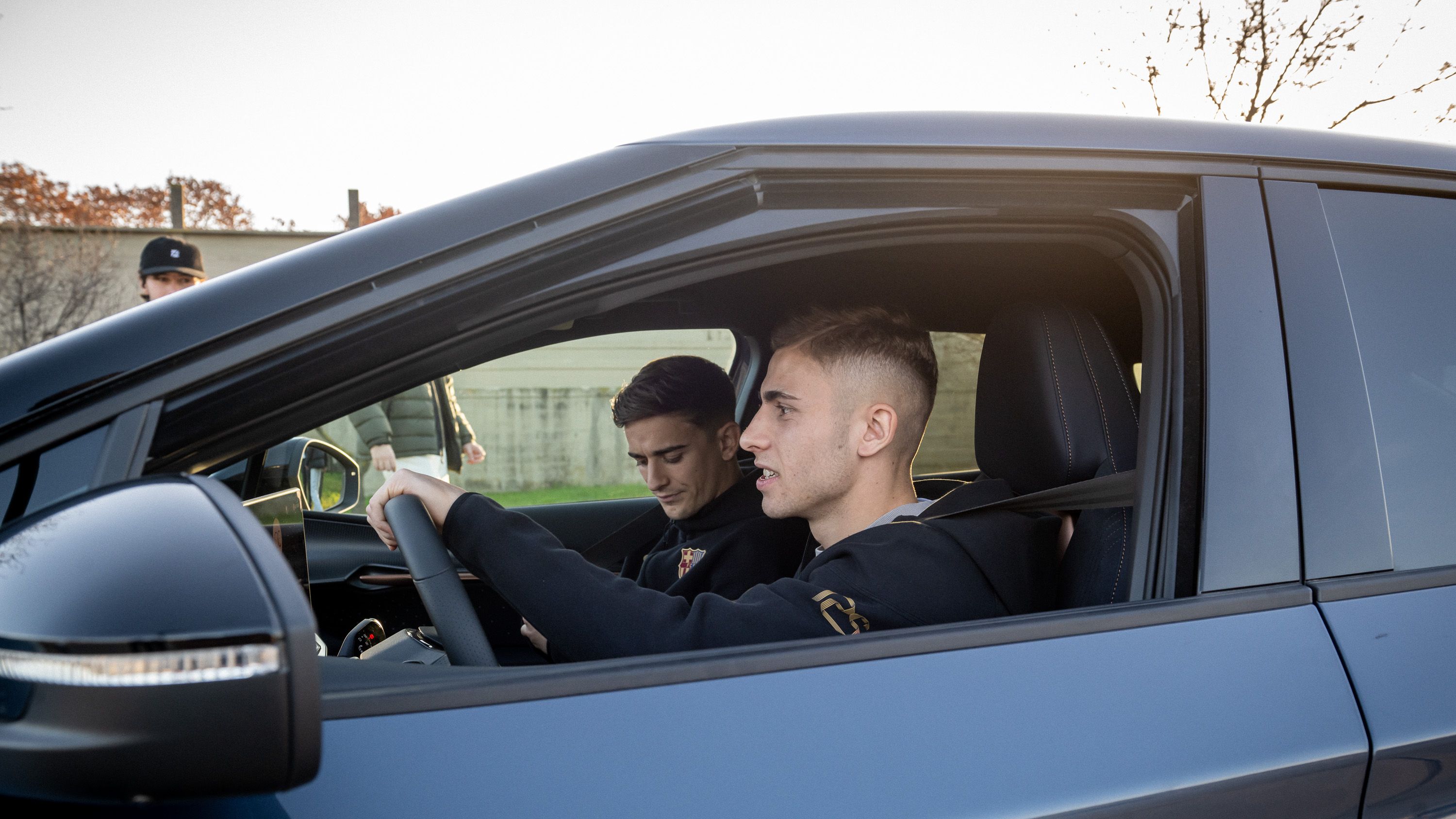 Dva igralca kluba Barcelona sedita v avtomobilu CUPRA Terramar, eden za volanom, drugi na sovoznikovem sedežu. Avtomobil je moder, z zasenčenimi stekli. 