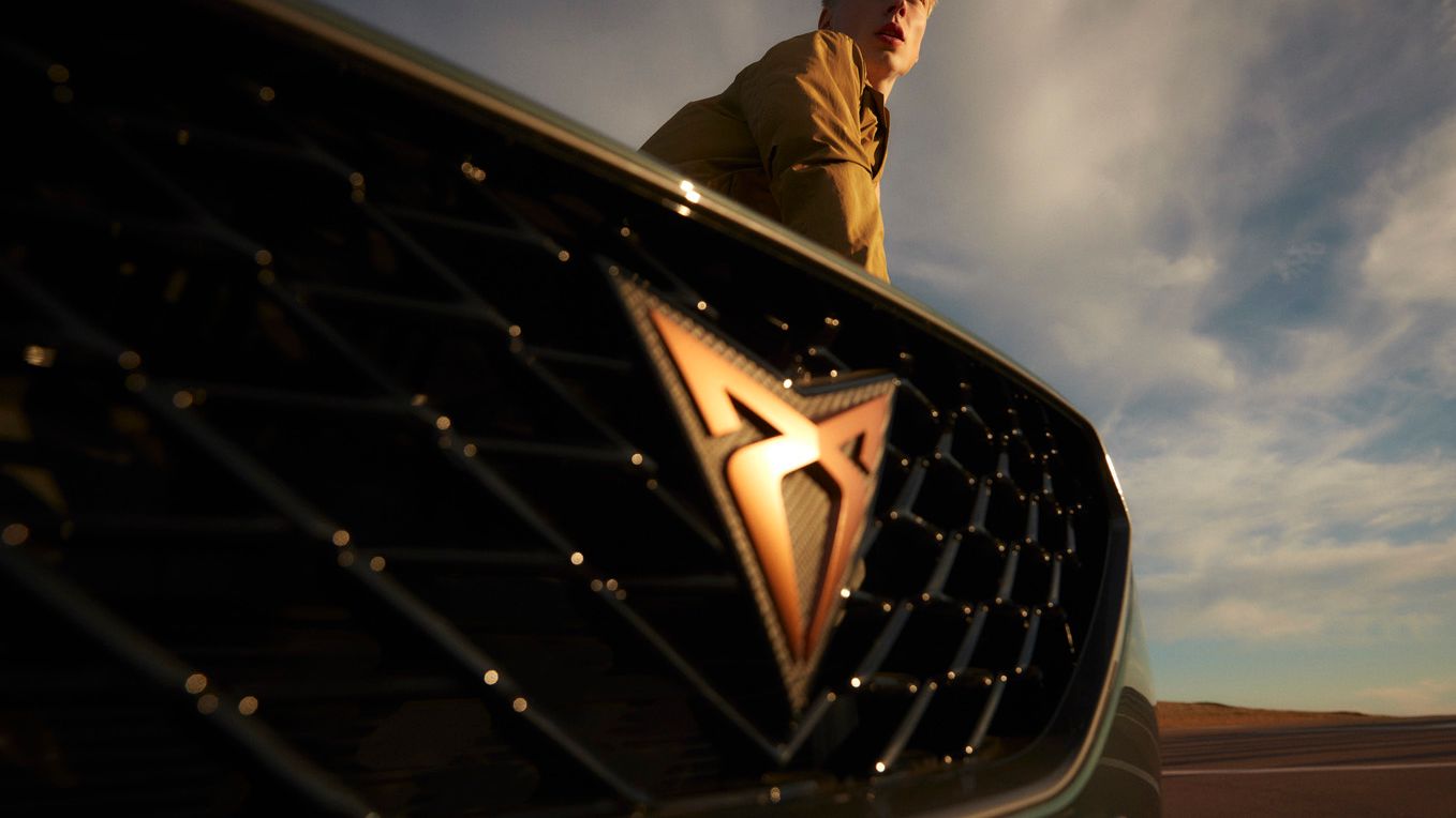 Moški stoji za avtomobilom CUPRA Formentor na katerem se jasno vidi logo znamke. Ozadje prikazuje modro-sive oblake na nebu.