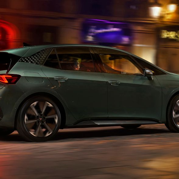 CUPRA Born VZ v temno zeleni barvi vozi po mestni ulici ponoči, osvetljeni z uličnimi lučmi. Ozadje vključuje zgradbe in trgovinske izložbe. Kolesa avtomobila so v gibanju.