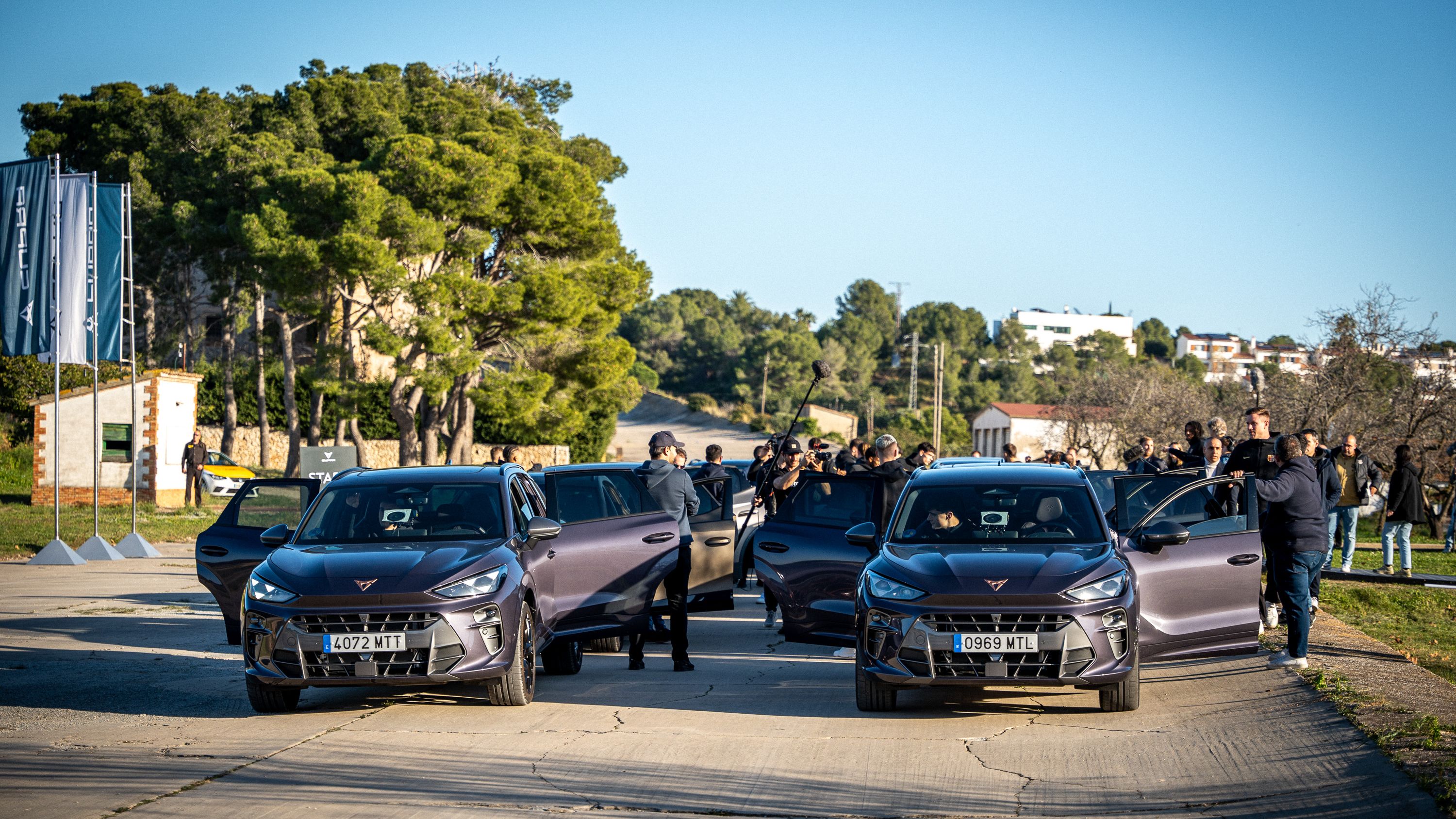 Na sliki so štirje avtomobili znamke CUPRA parkirani na prostem. Skupina ljudi stoji ob avtomobilih, nekateri imajo kamere. V ozadju so drevesa in stavbe.