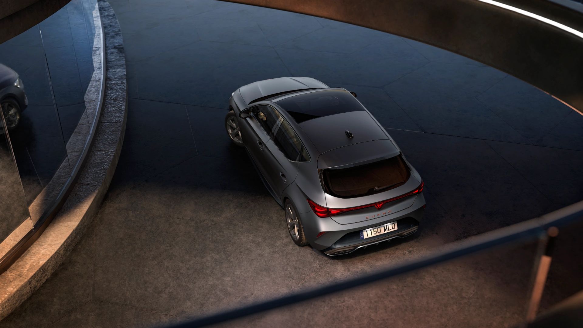 CUPRA Leon, slikan iz ptičje perspektive in iz zadnje strani. Parkiran je na ovinkasti cesti v garaži.