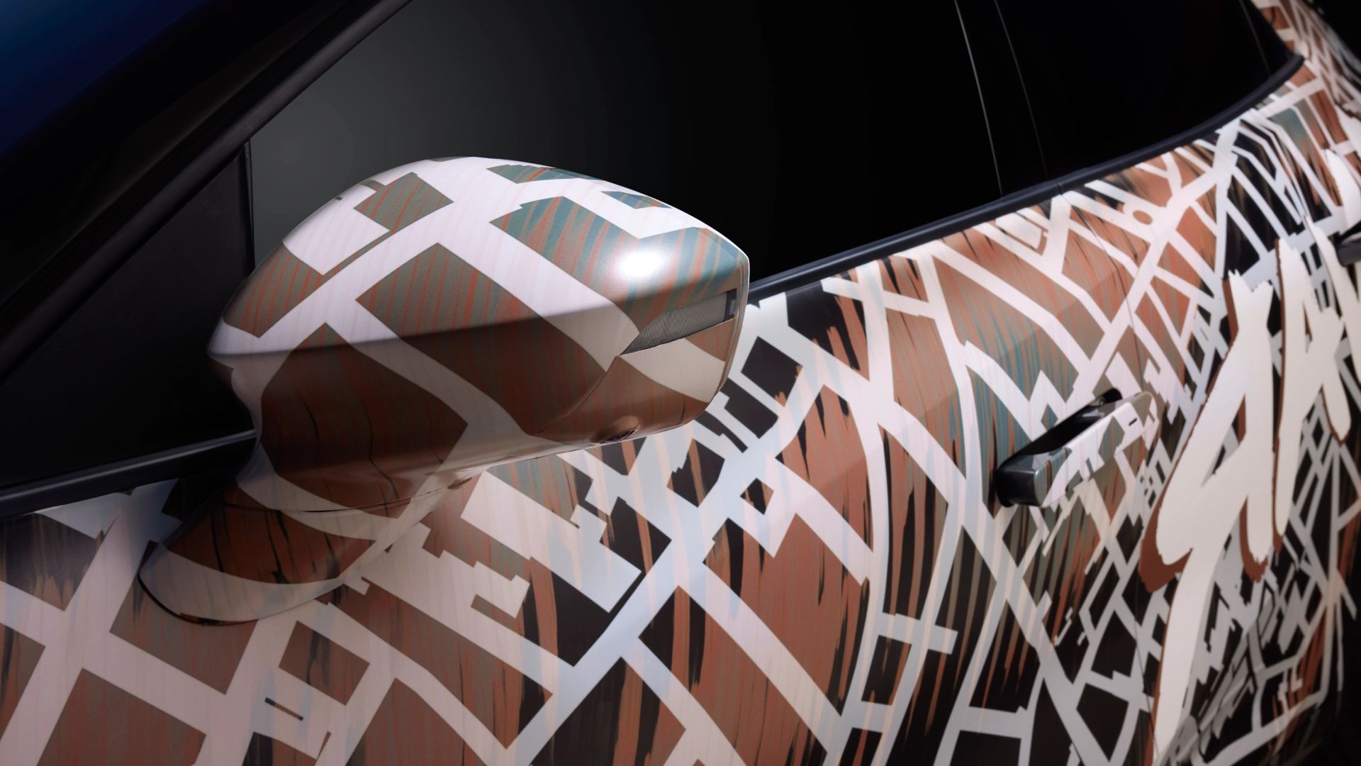 Od blizu prikazan bočno ogledalo avtomobila CUPRA Raval Dynamic, ki je delno prekrito z vzorcem grafičnih črt in oblik v rjavi, beli in črni barvi. Ozadje je zamegljeno.