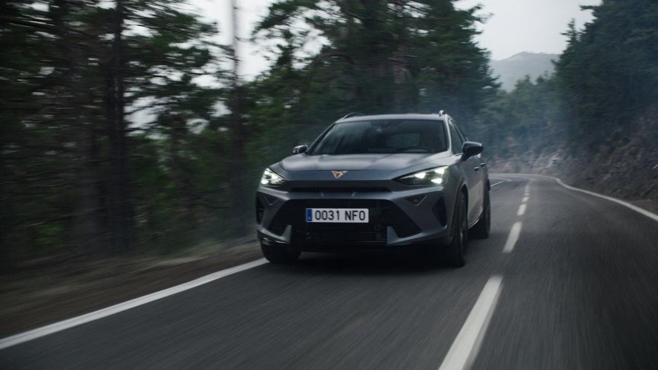 Cupra Formentor vozi po ovinkasti gozdni cesti v naravnem okolju. Dinamičen prizor poudarja zmogljivost in stabilnost vozila med vožnjo.