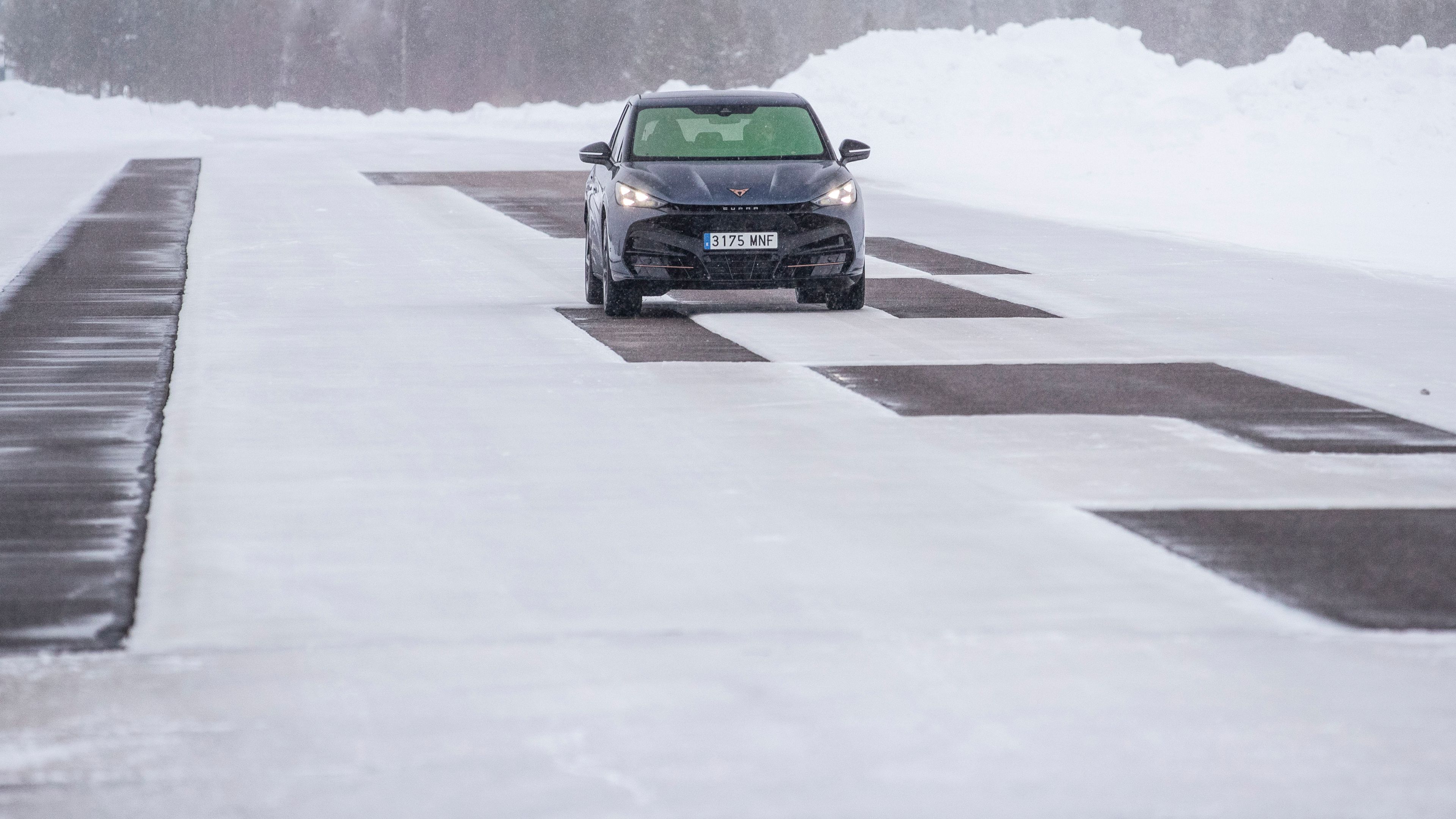 CUPRA Tavascan vozi po zasneženi cesti, obdan z zasneženo pokrajino in drevesi v ozadju.