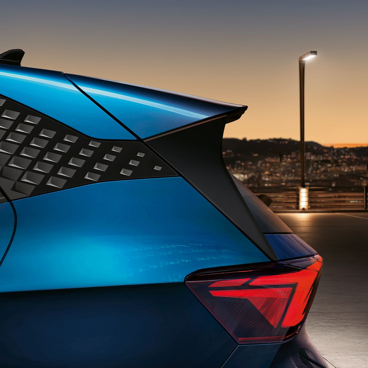 Modra športna limuzina Cupra Born je parkirana zunaj v mestu ob mraku. Zadnji del avtomobila razkriva moderno obliko z agresivno linijo strehe.