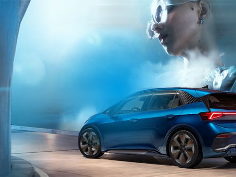 Cupra Born, modra športna limuzina vozi skozi moder tunel. V ozadju je voda, ki se dviga v zrak. V zgornjem desnem kotu je bel logo podoben puščici.