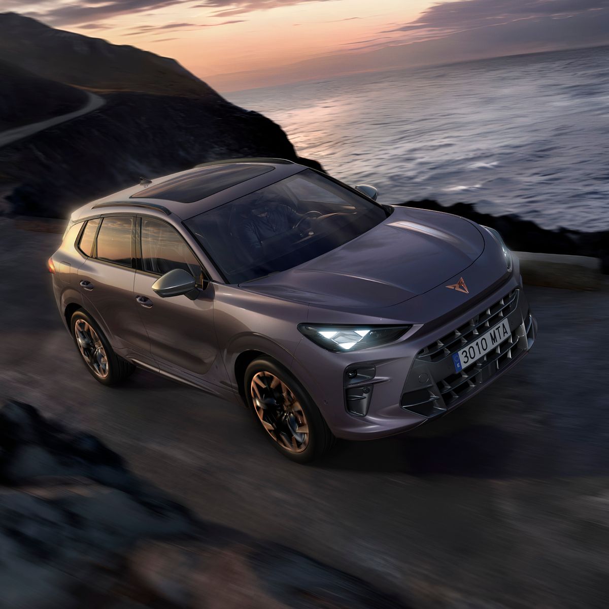 CUPRA Terramar sive barve vozi po obalni cesti ob sončnem zahodu.