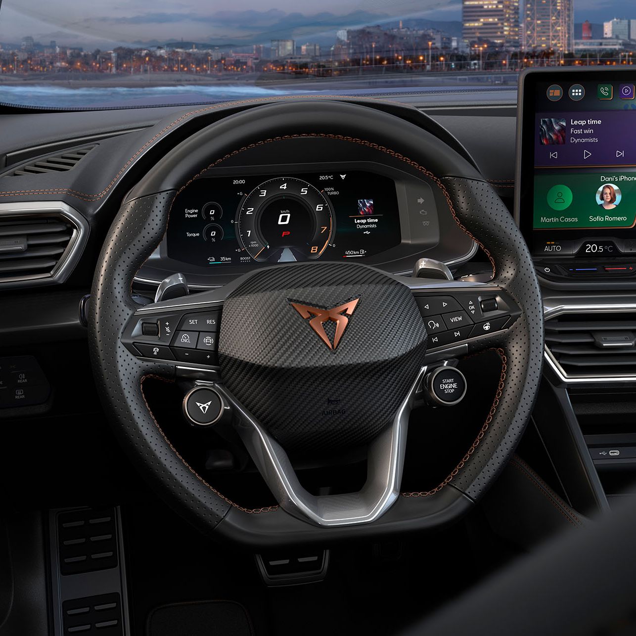 Notranjost avtomobila Cupra Formentor prikazuje volan znamke Cupra ter del armaturne plošče z dvema digitalnima zaslonoma. Zaslon na volanu prikazuje informacijski sistem avtomobila, medtem ko desni zaslon prikazuje navigacijo. V ozadju je pogled na mesto ob morju.