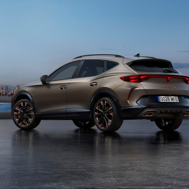 CUPRA Formentor PA, parkiran ob obali ob sončnem vzhodu, z mestom v ozadju v modrikasti svetlobi.