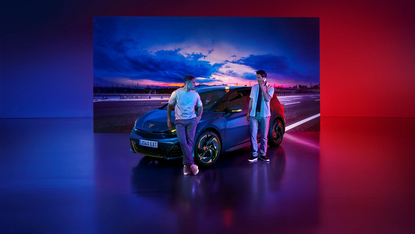 Dva človeka stojita ob avtomobilu CUPRA Born, parkiranem v studiu z osvetljenim nebesnim ozadjem. Osvetlitev je modro-rdeča, kar ustvarja futurističen občutek.