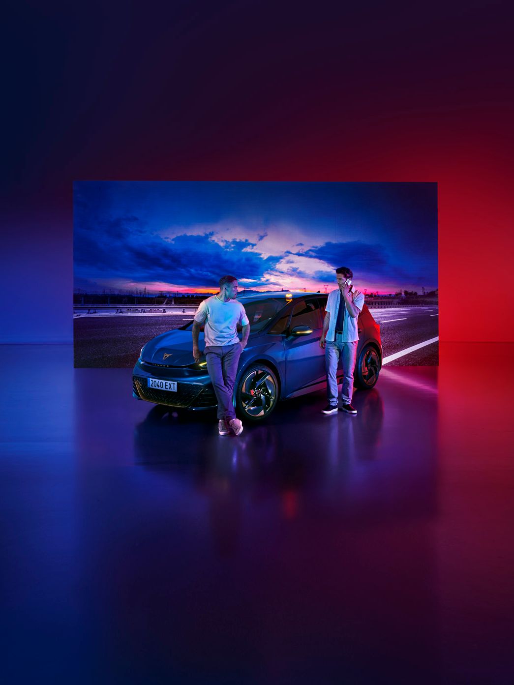 Dva človeka stojita ob avtomobilu CUPRA Born, parkiranem v studiu z osvetljenim nebesnim ozadjem. Osvetlitev je modro-rdeča, kar ustvarja futurističen občutek.