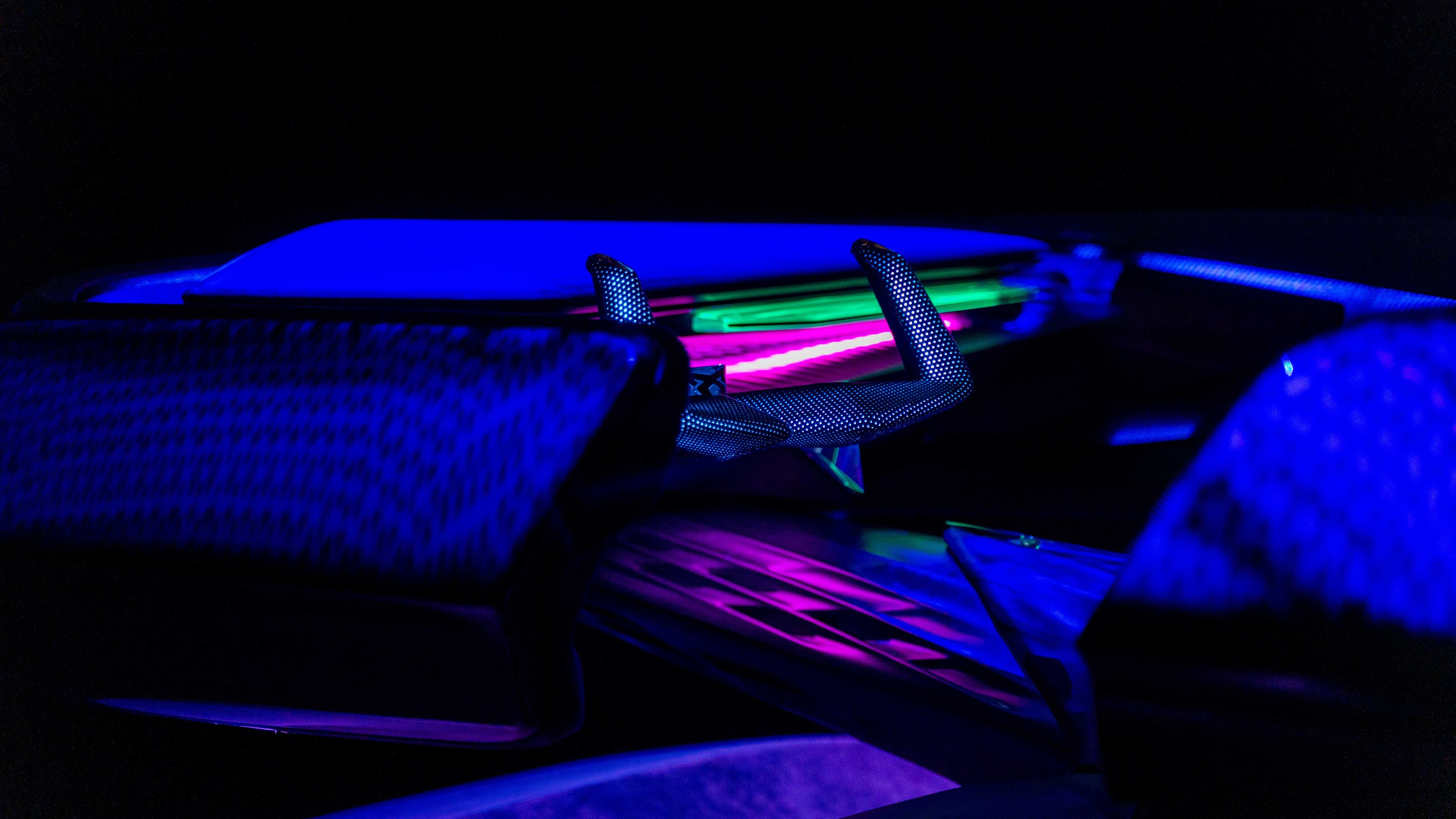 Sodobno osvetljena notranjost futurističnega avtomobila znamke CUPRA z intenzivno modro in vijolično razsvetljavo. Volan in sedeži so tehnologijsko oblikovani in poudarjeni s svetlobnimi efekti. 