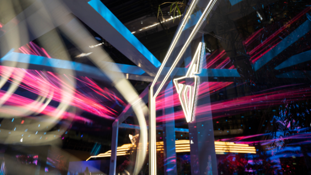 Umetniško zamegljena nočna fotografija z osvetljenimi neonskimi lučmi in logotipom znamke CUPRA. 