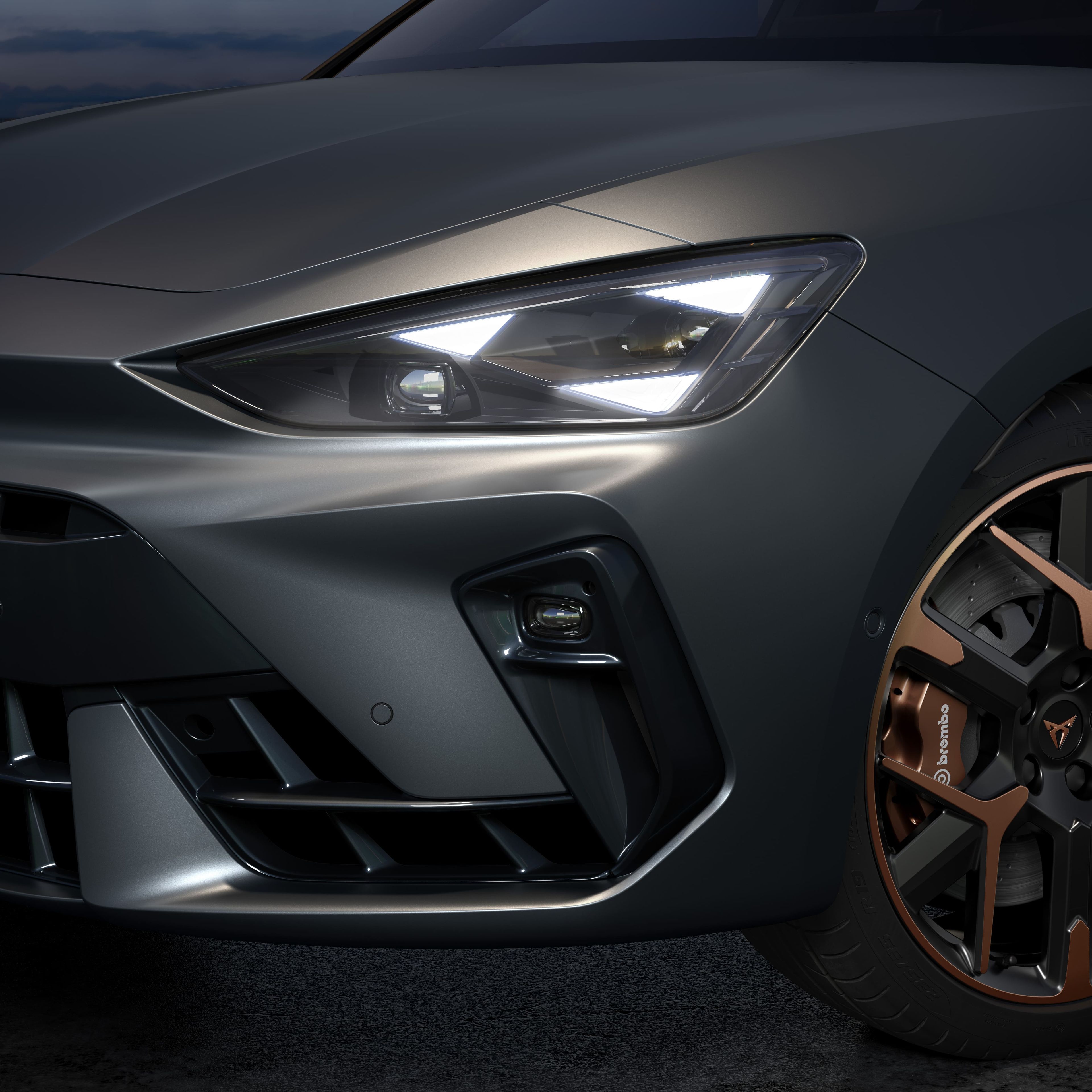 Detajlni posnetek sprednjega dela elegantnega avtomobila CUPRA Leon PA z impresivnimi lučmi in edinstvenimi rjavo-črnimi platišči. Avto je parkiran v zunanji okolici ob mraku.