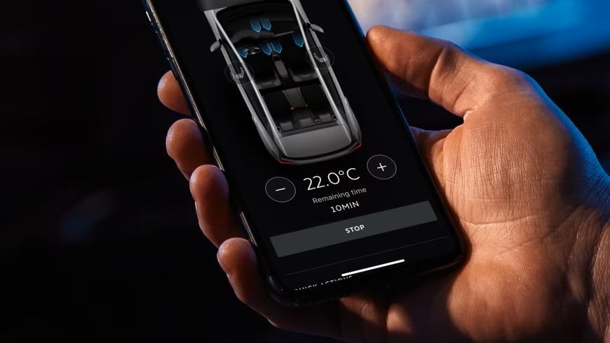 Roka drži pametni telefon, ki na zaslonu prikazuje aplikacijo 'My CUPRA app' za nadzor klimatske naprave v avtomobilu. Temperatura je nastavljena na 22°C. V ozadju je zamegljen avtomobil CUPRA Born.