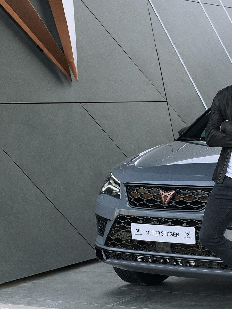 Marc ter Stegen, ki je postal uradni ambasador znamke CUPRA stoji pred CUPRA vozilom. Vozilo je parkirano pred moderno arhitekturno strukturo.