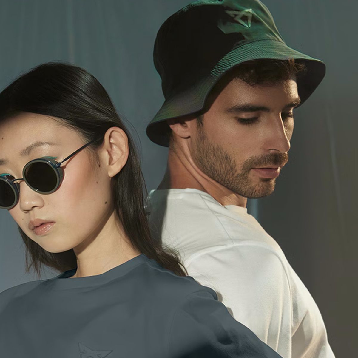 Ena oseba nosi temno majico in modna očala kolekcije CUPRA COLLECTION. Druga oseba pa belo majico in klobuk. Naslonjeni sta s hrbtoma.