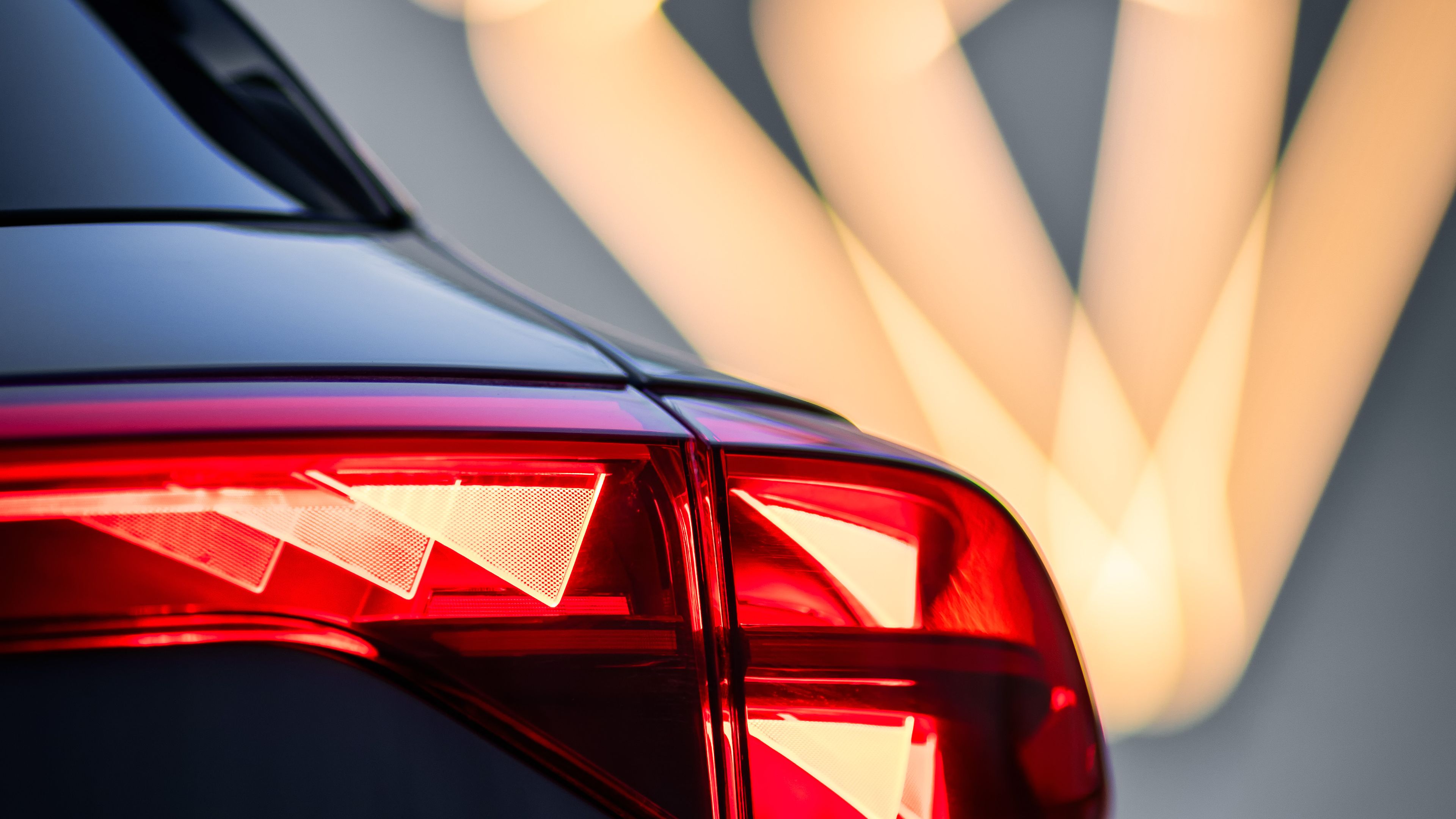 Zadnji del avtomobila CUPRA Terramar z vklopljenim zadnjim lučmi. V ozadju je svetleči logotip znamke. 